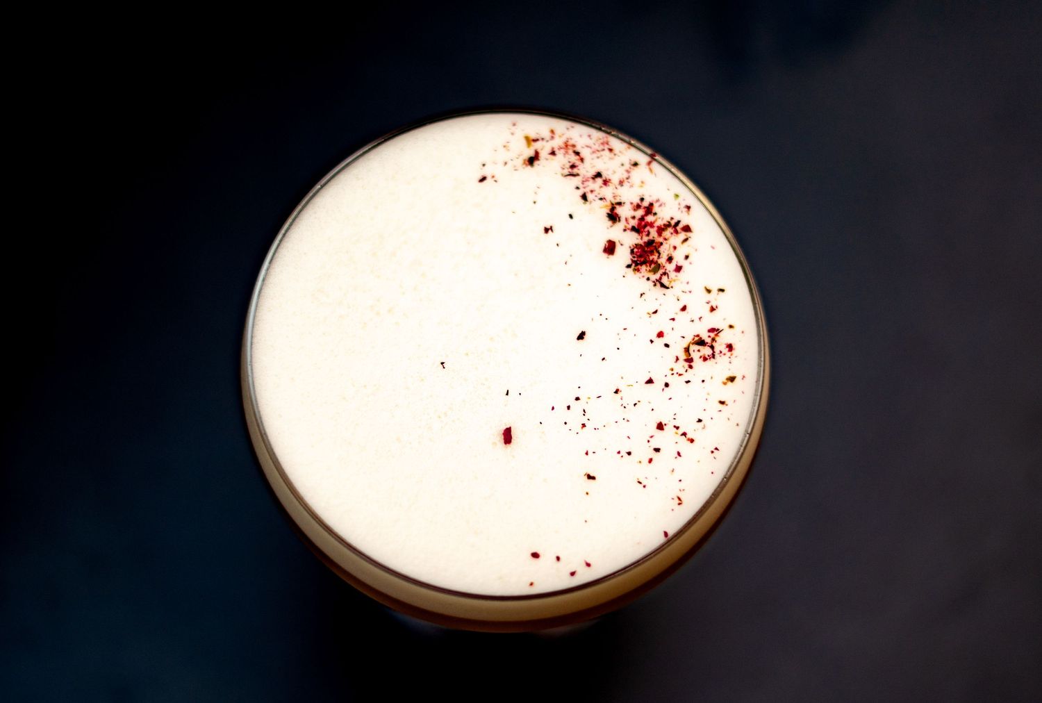 Overhead view of a white cocktail with red spice garnish in a coupe glass.