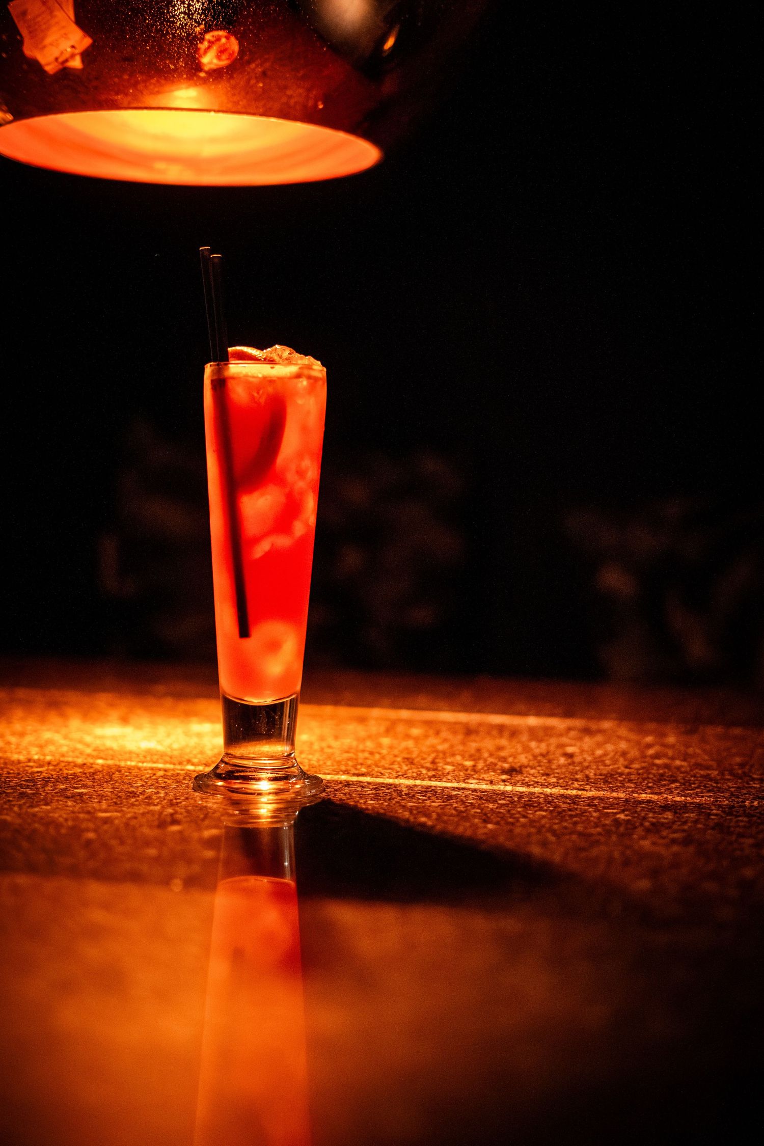 A tall cocktail glass illuminated by dramatic orange lighting from above.