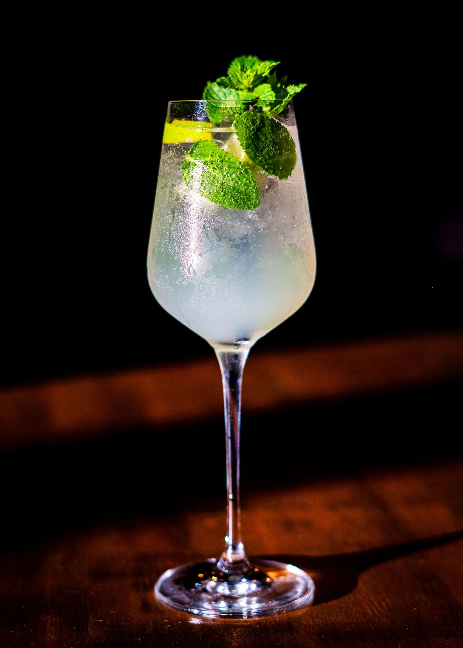 Elegant cocktail with fresh mint garnish in a stemmed glass on wooden surface.