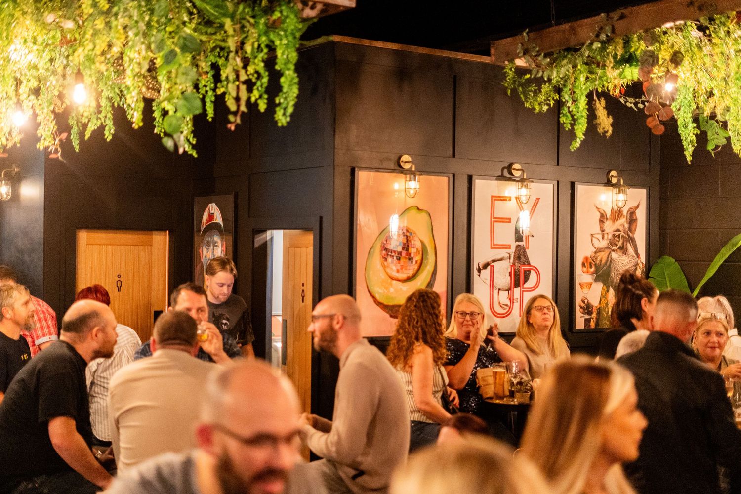 Restaurant interior featuring hanging greenery and decorative lighting above a busy dining area.