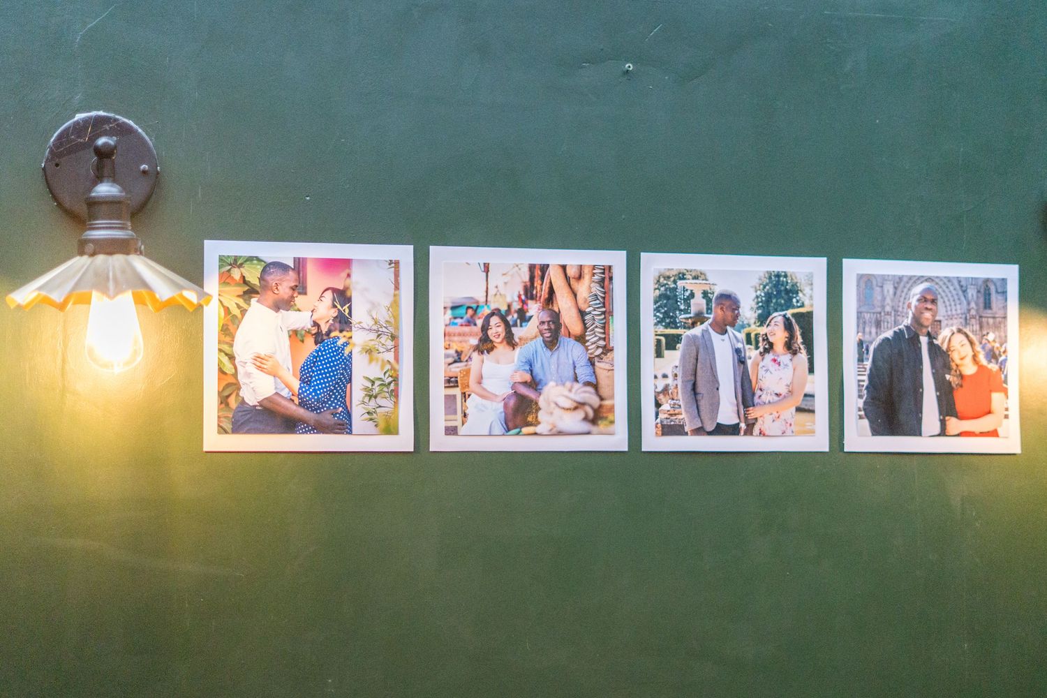 Row of framed photographs displayed on a green wall with pendant lighting.