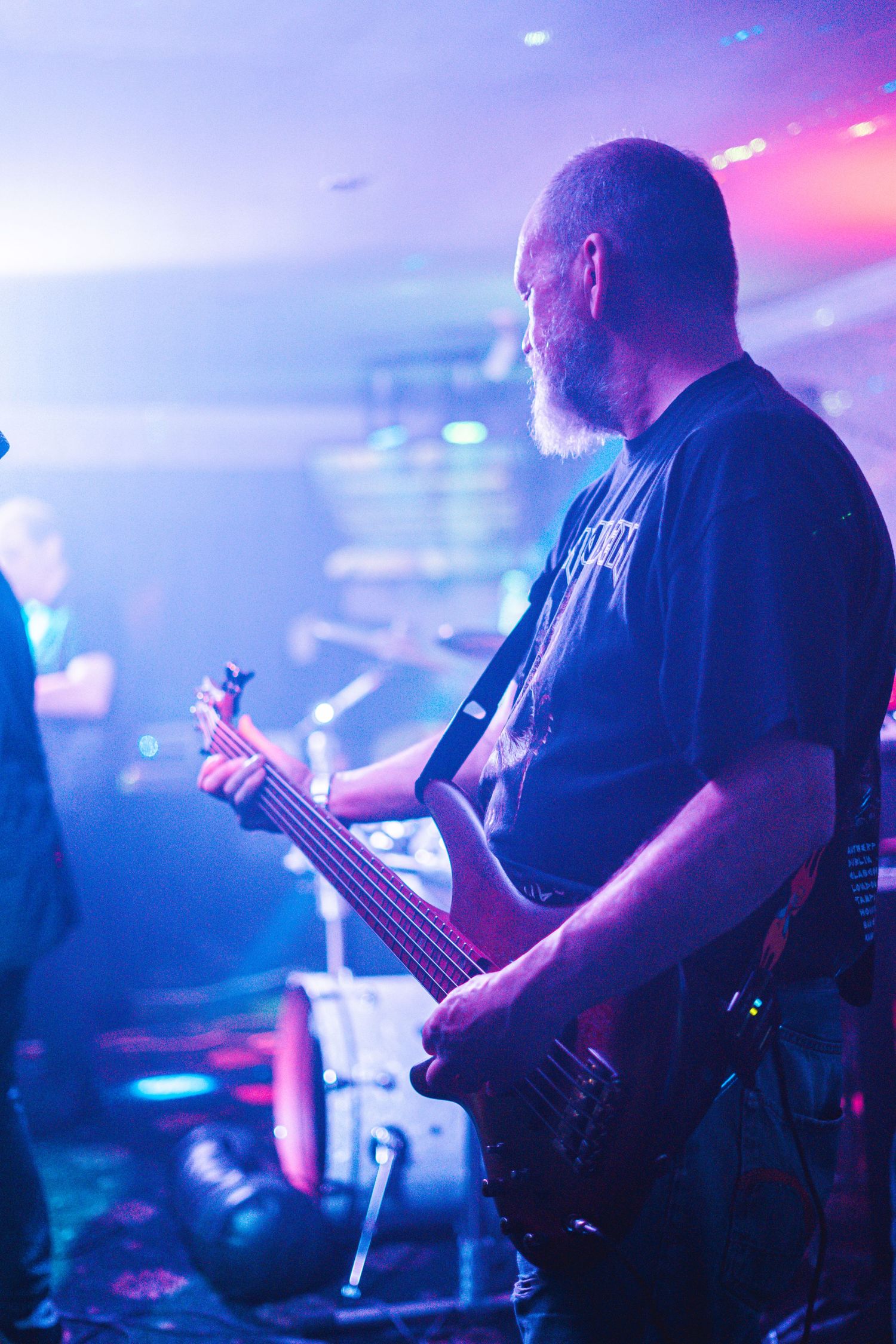 Bass guitarist performs on stage illuminated by purple and blue stage lights.
