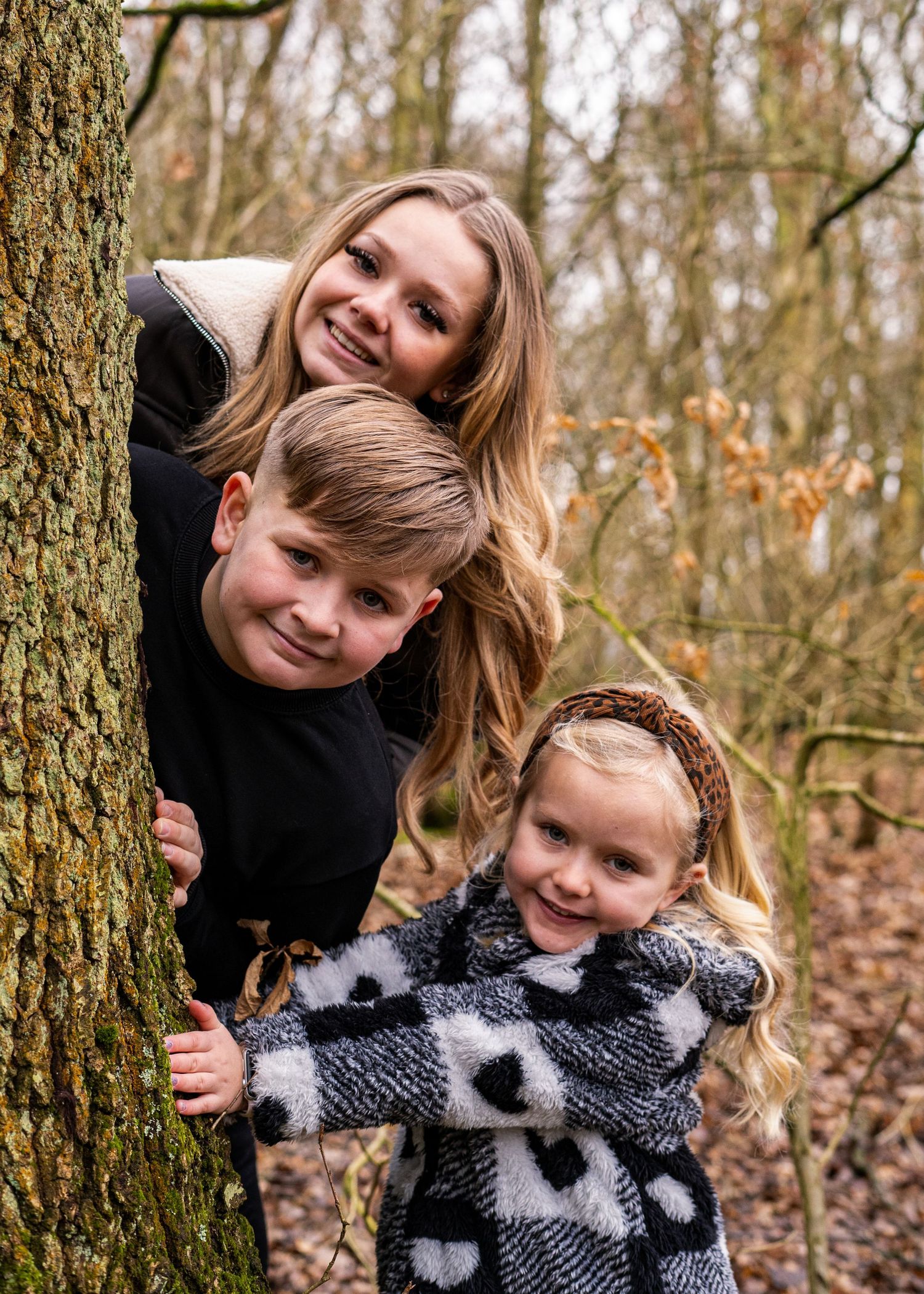 Playful peek-a-boo moment between family members around a tree trunk.