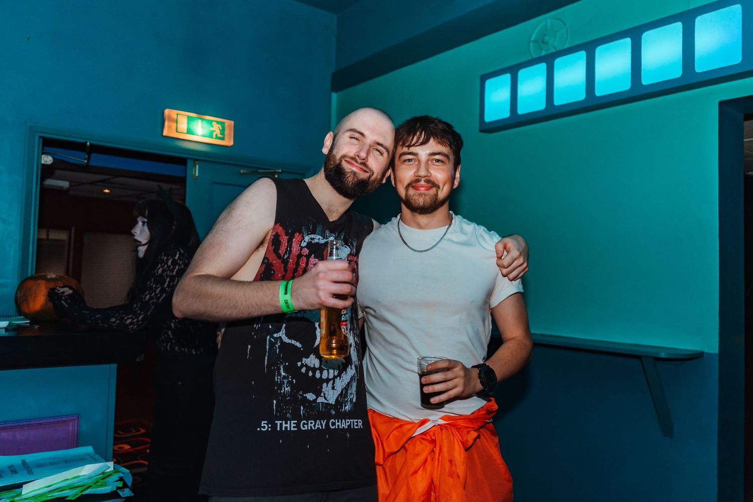 Two friends sharing drinks and smiles at a club with blue lighting.