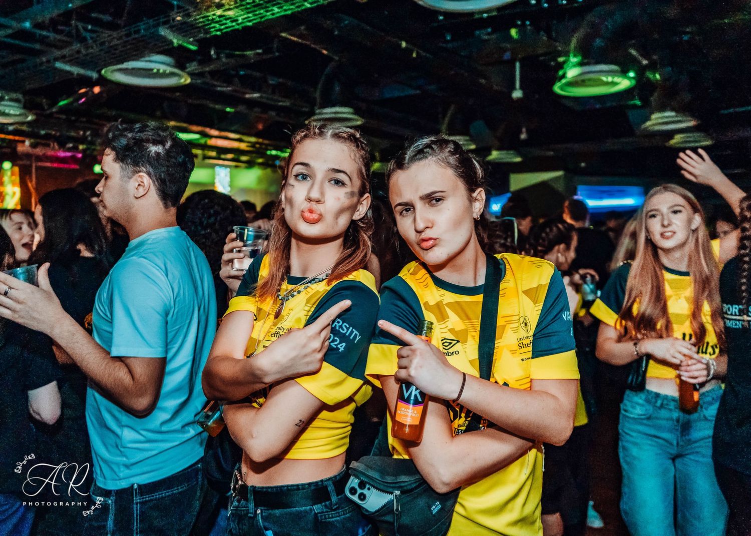 Party crowd wearing yellow and black outfits dancing at a nightclub event.
