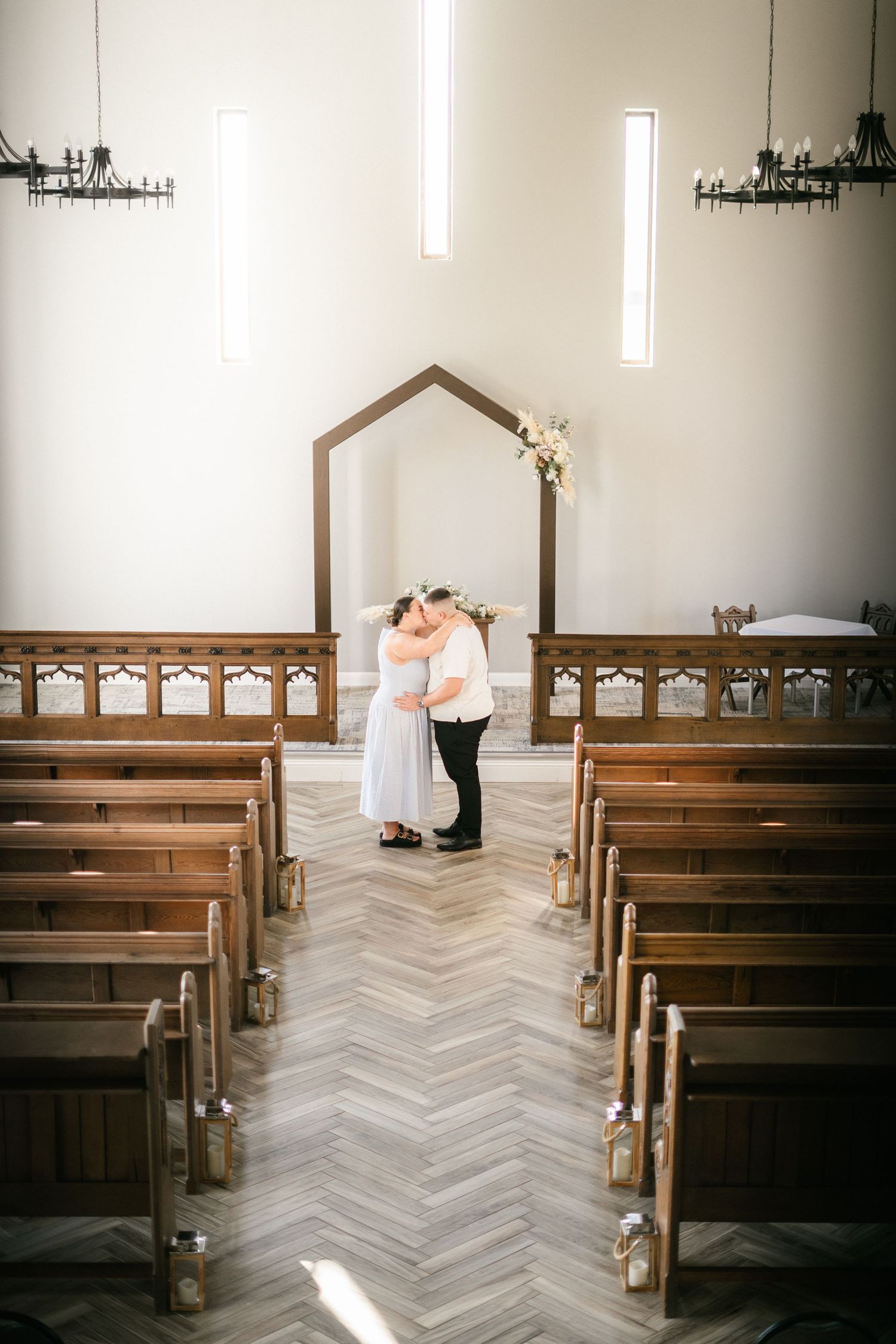 Elegant church interior with wooden pews and herringbone pattern flooring in a minimalist white chapel.