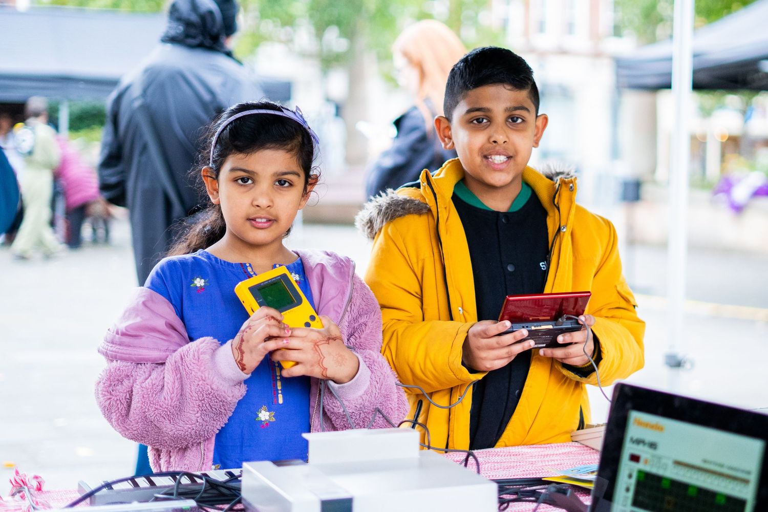 Two young people in colorful jackets holding electronic devices at an outdoor event.
