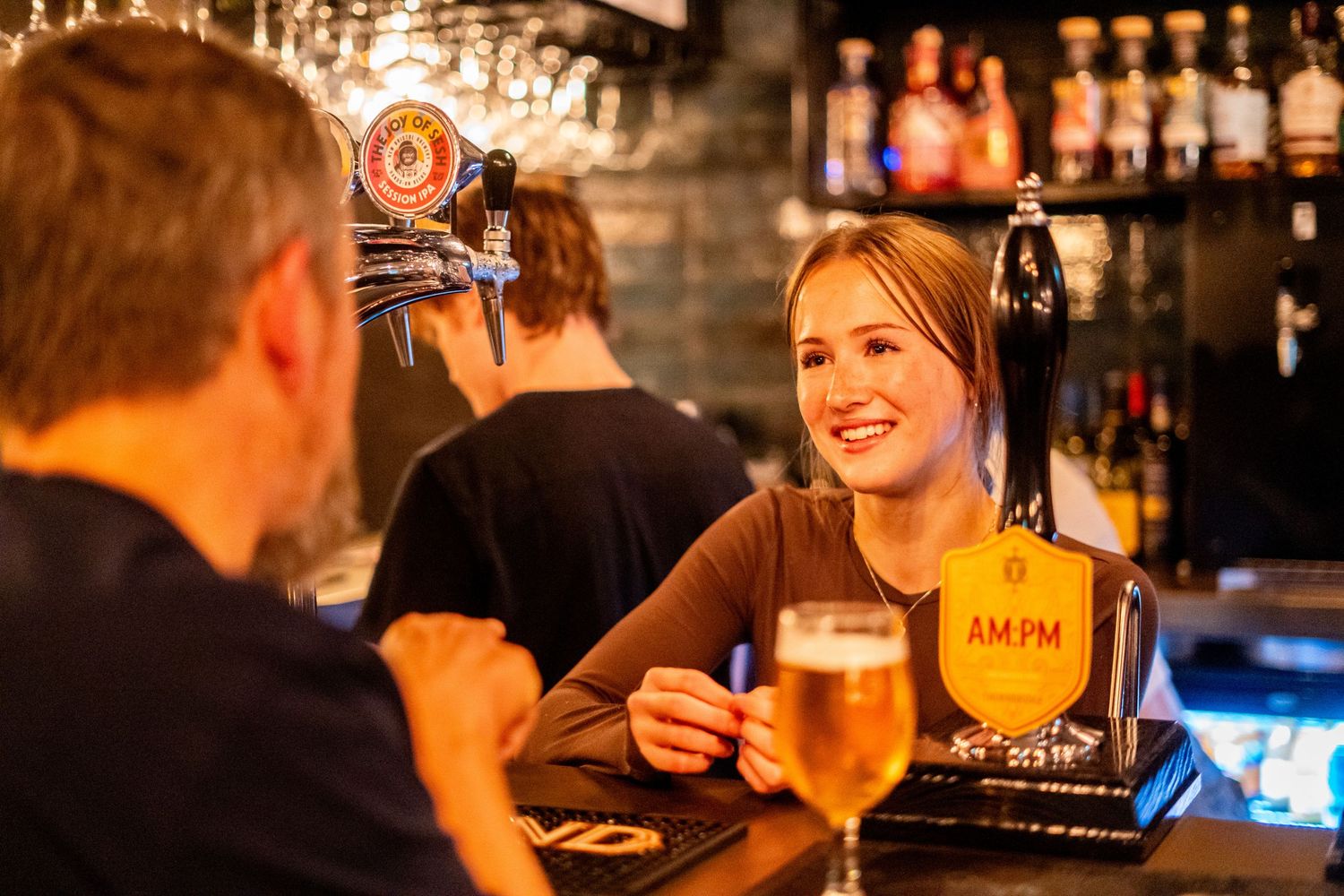 Bar scene with draft beer taps and bottles displayed on shelves in warm lighting.