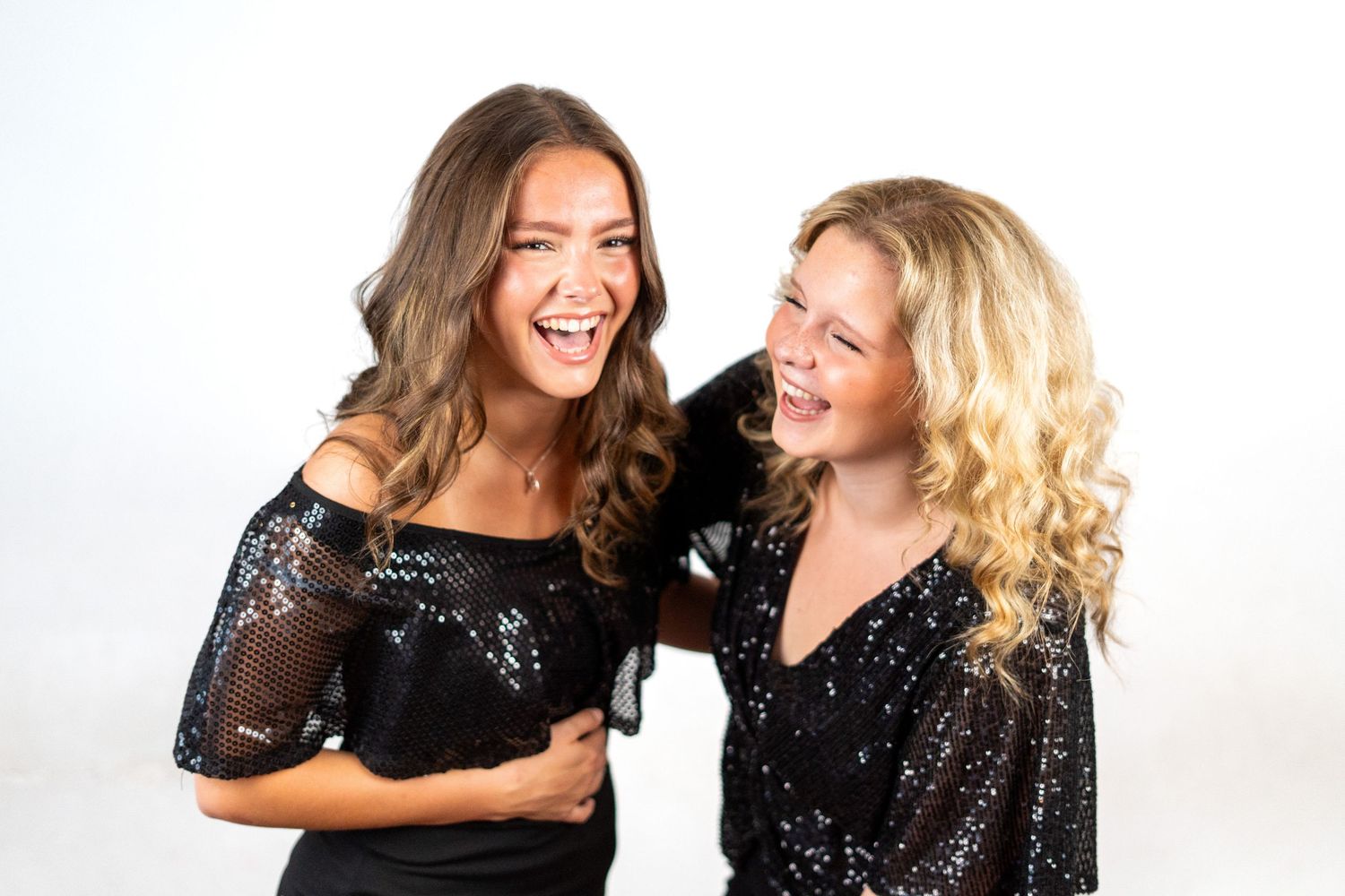 Two people in sparkly black outfits laughing together against white background.