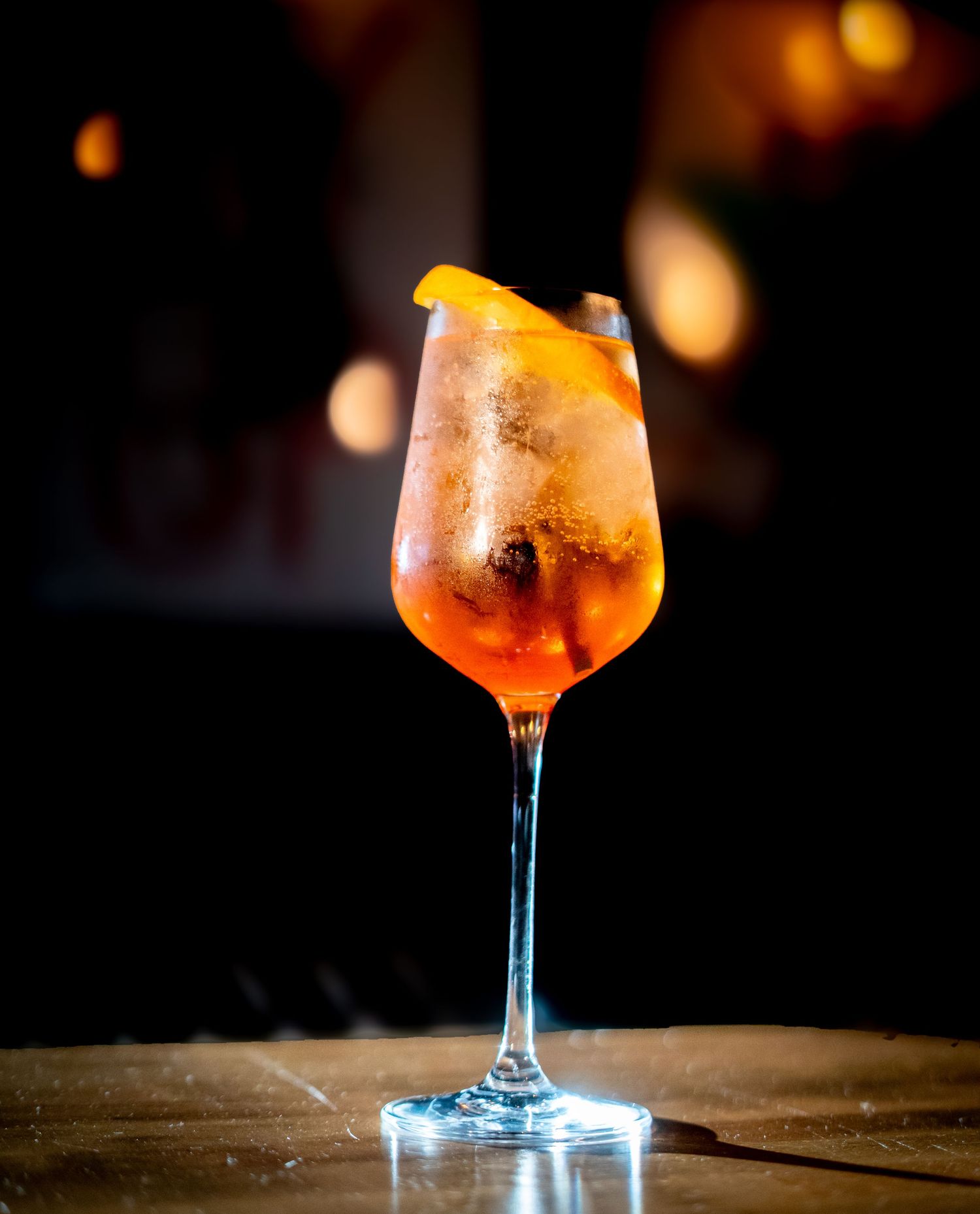 Elegant spritz cocktail with orange garnish served in wine glass on dark surface.