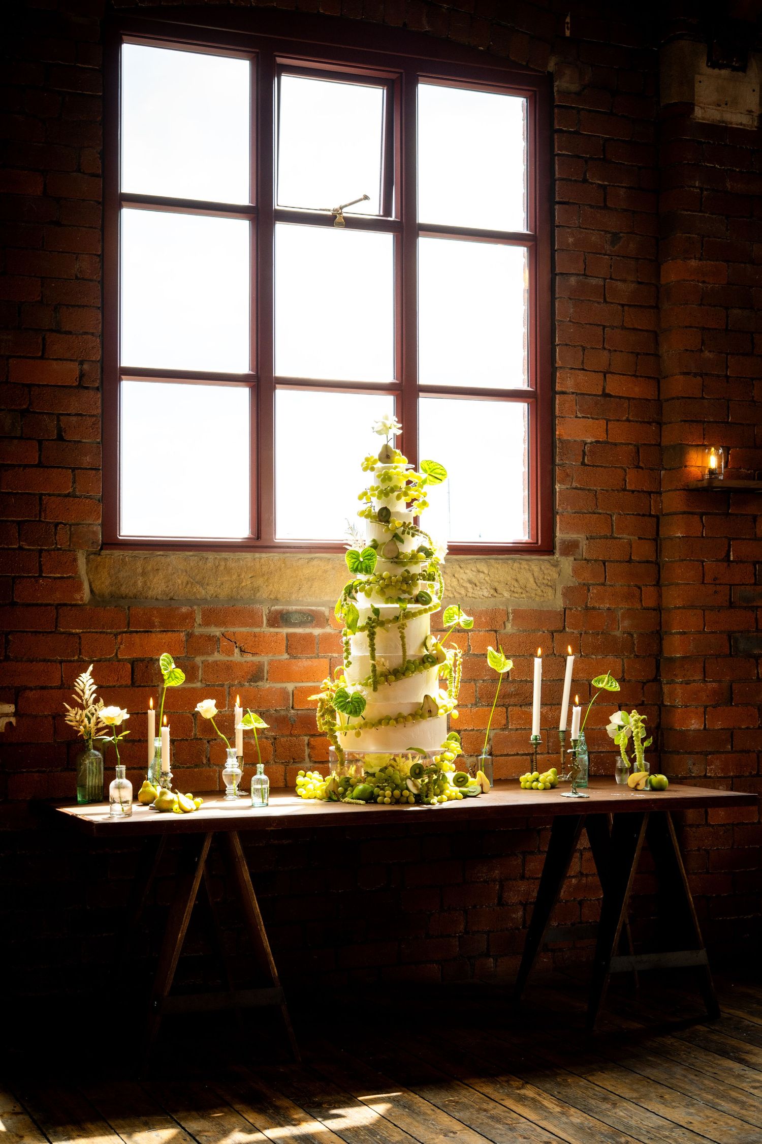 Sunlit wedding cake setup in an industrial space with exposed brick walls and wooden flooring.