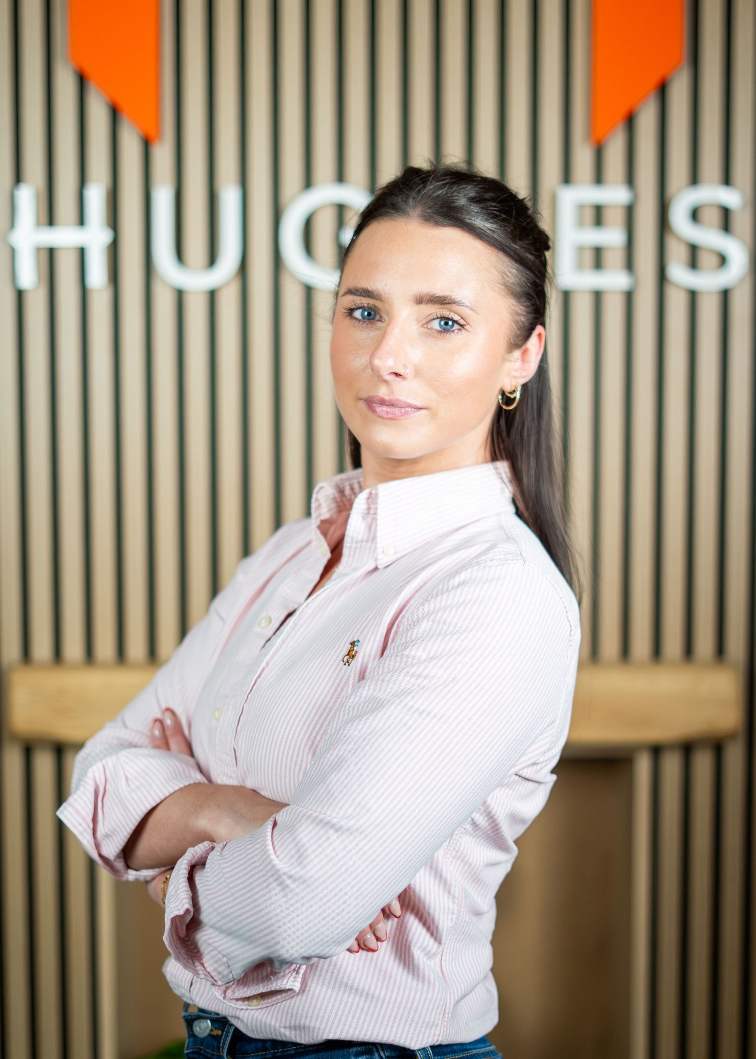 Professional in white button-down shirt poses against modern office wall with orange geometric design.