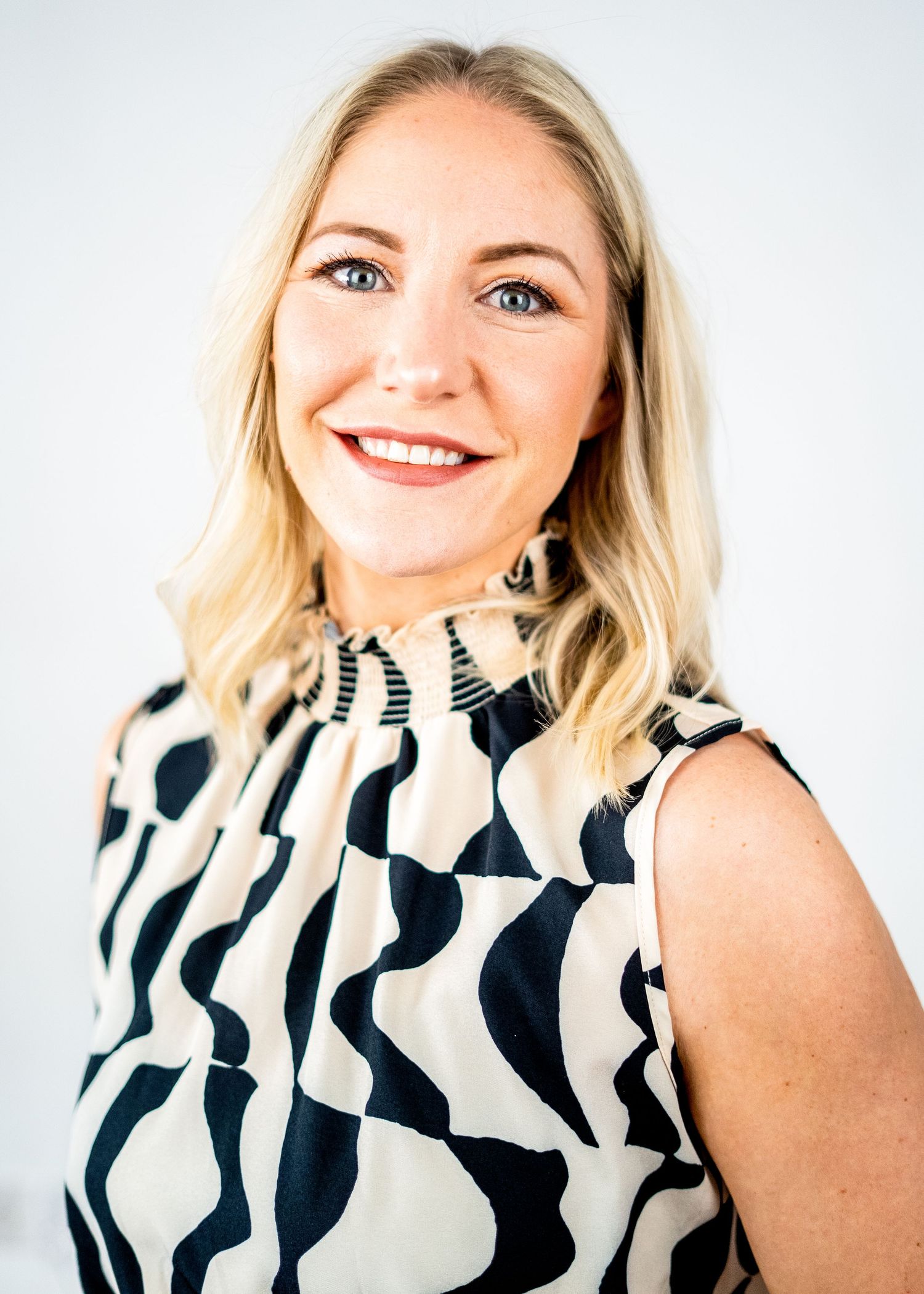 Portrait of a person in a black and white patterned sleeveless top with blonde hair.