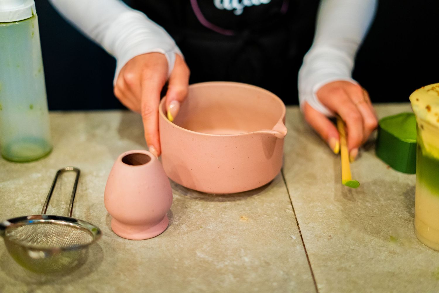 Hands working with pink ceramic bowls and food preparation tools on a gray counter.