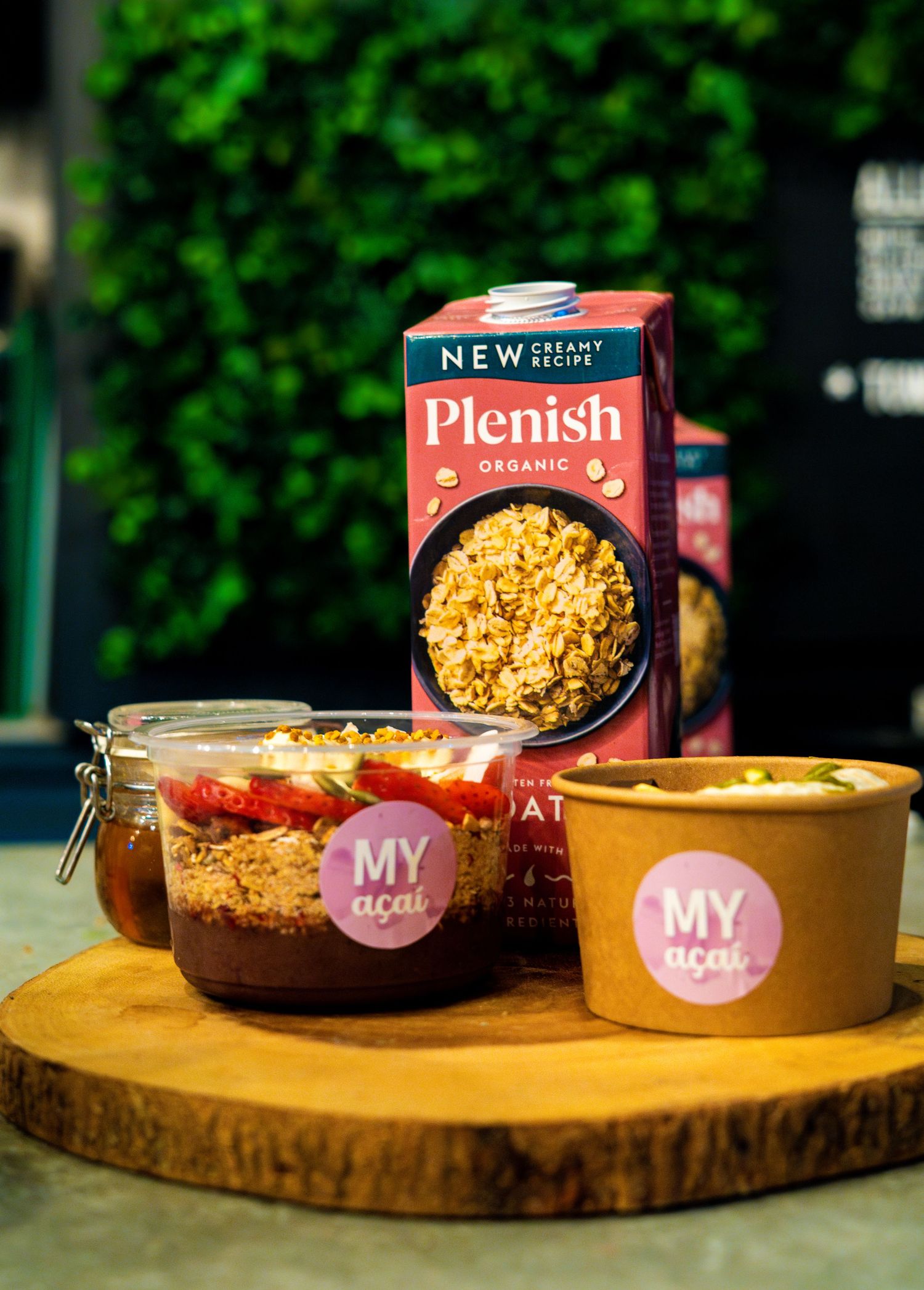 Food products and branded bowls displayed on a round wooden serving board with green background.