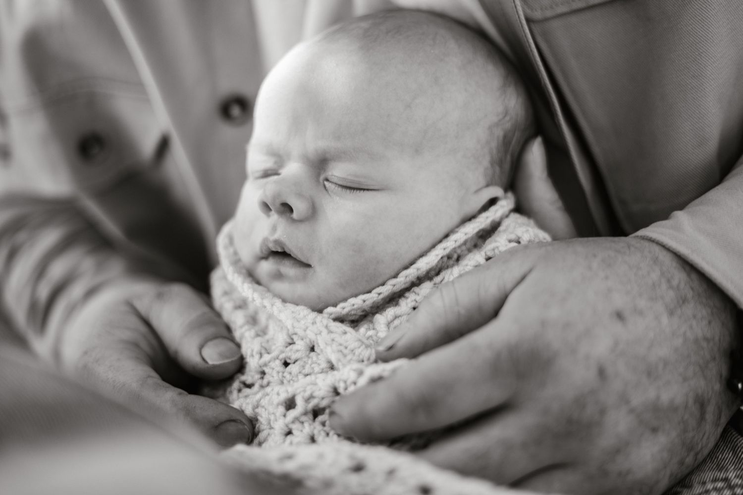 Black and white portrait of sleeping newborn wrapped in delicate knitted blanket.