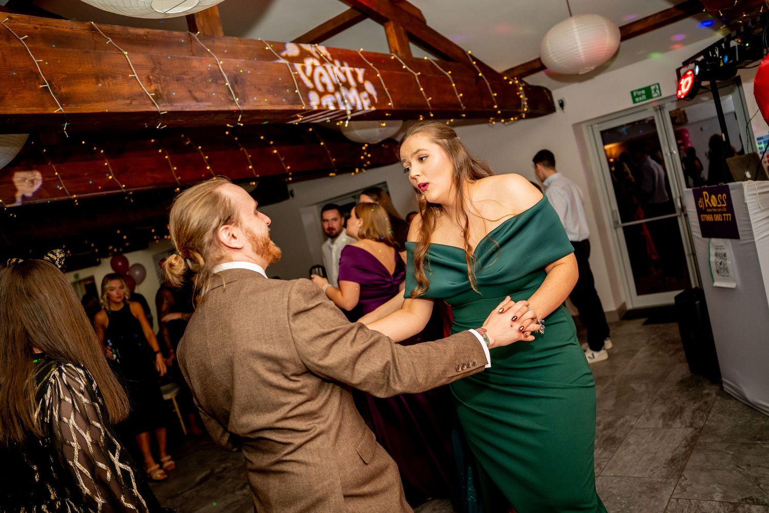 Couples dancing together at an indoor event with warm lighting and wooden ceiling beams.