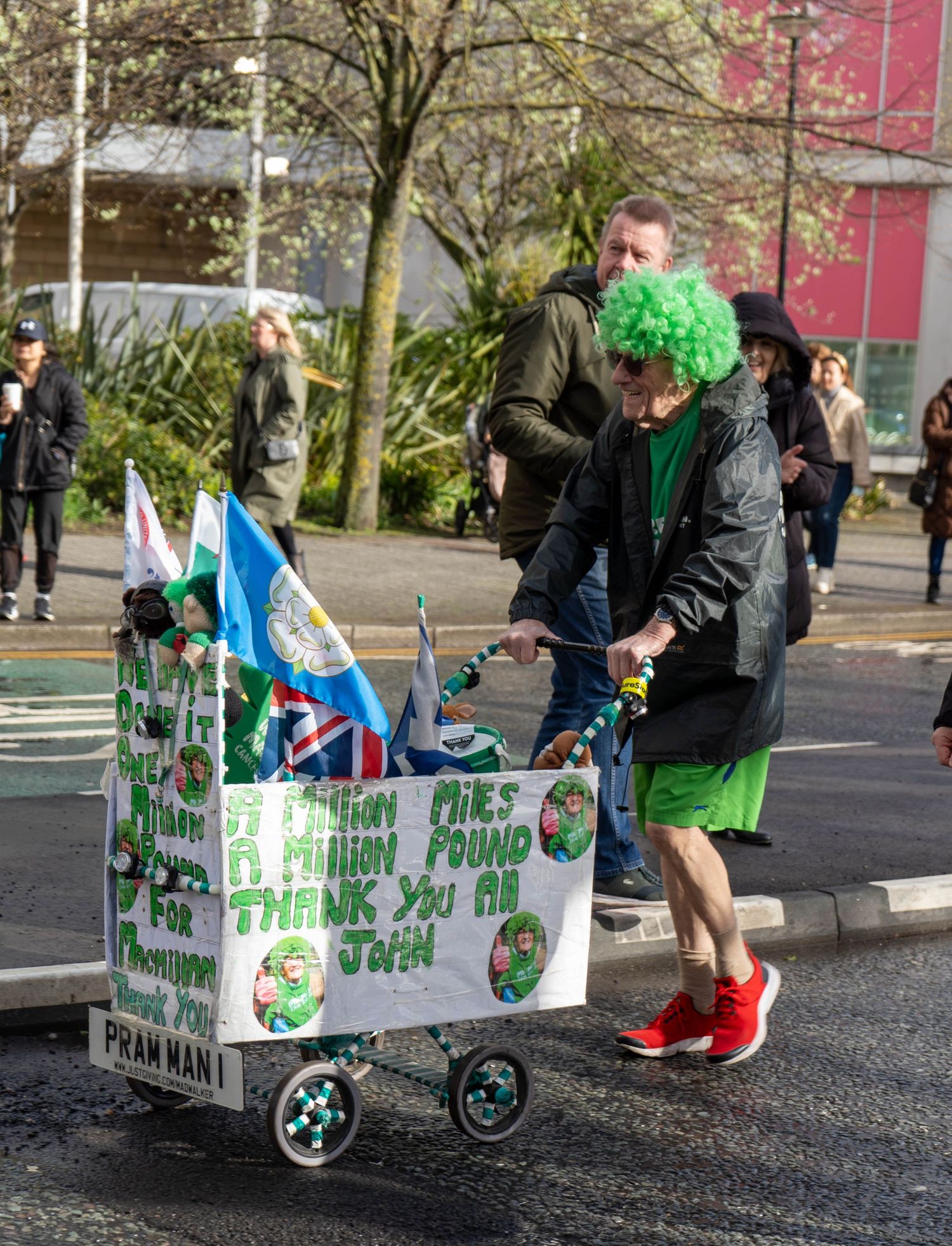 Supporter with green wig pushes decorated cart during charity race event.