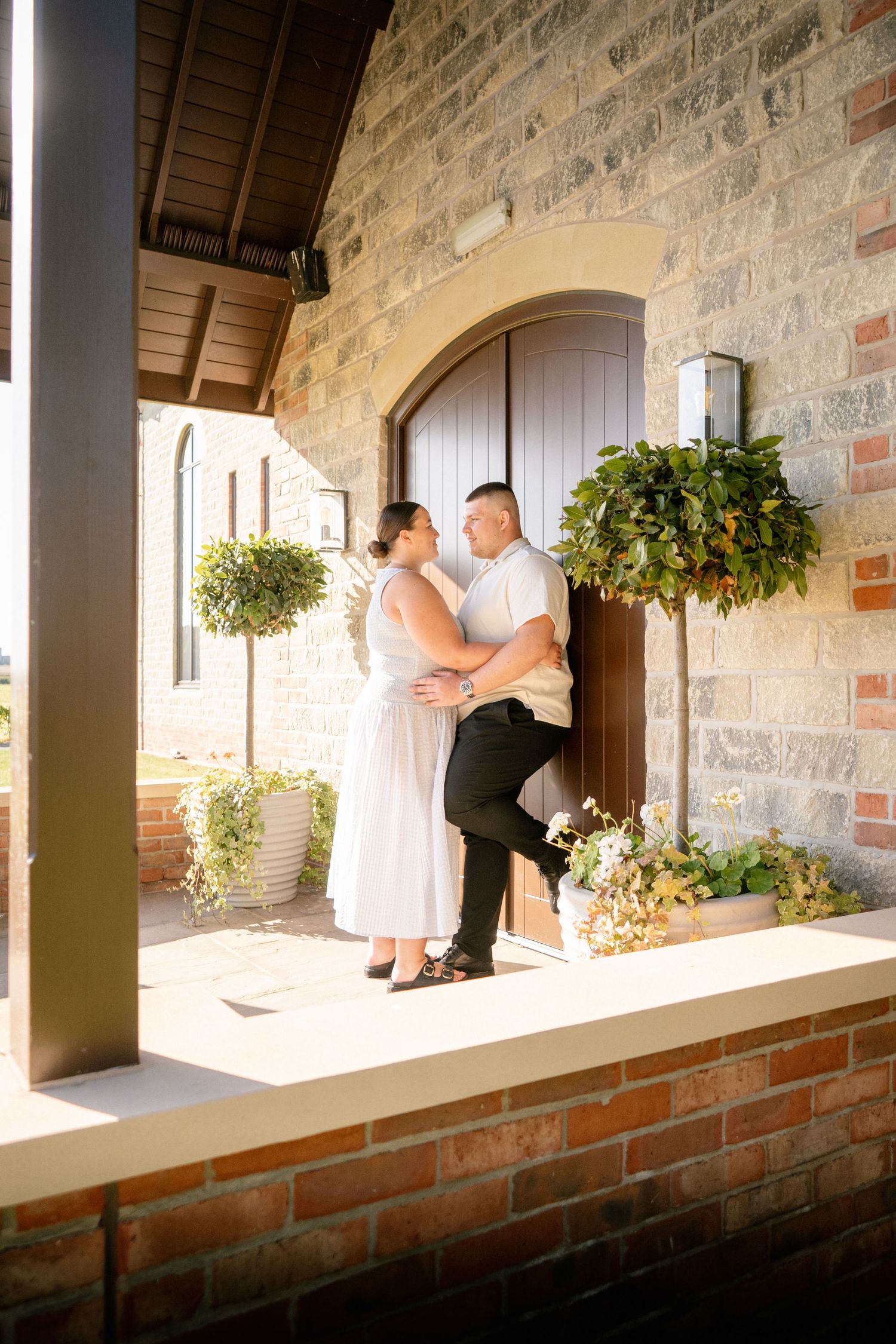 Stone archway with hanging plants frames couple sitting on brick ledge.