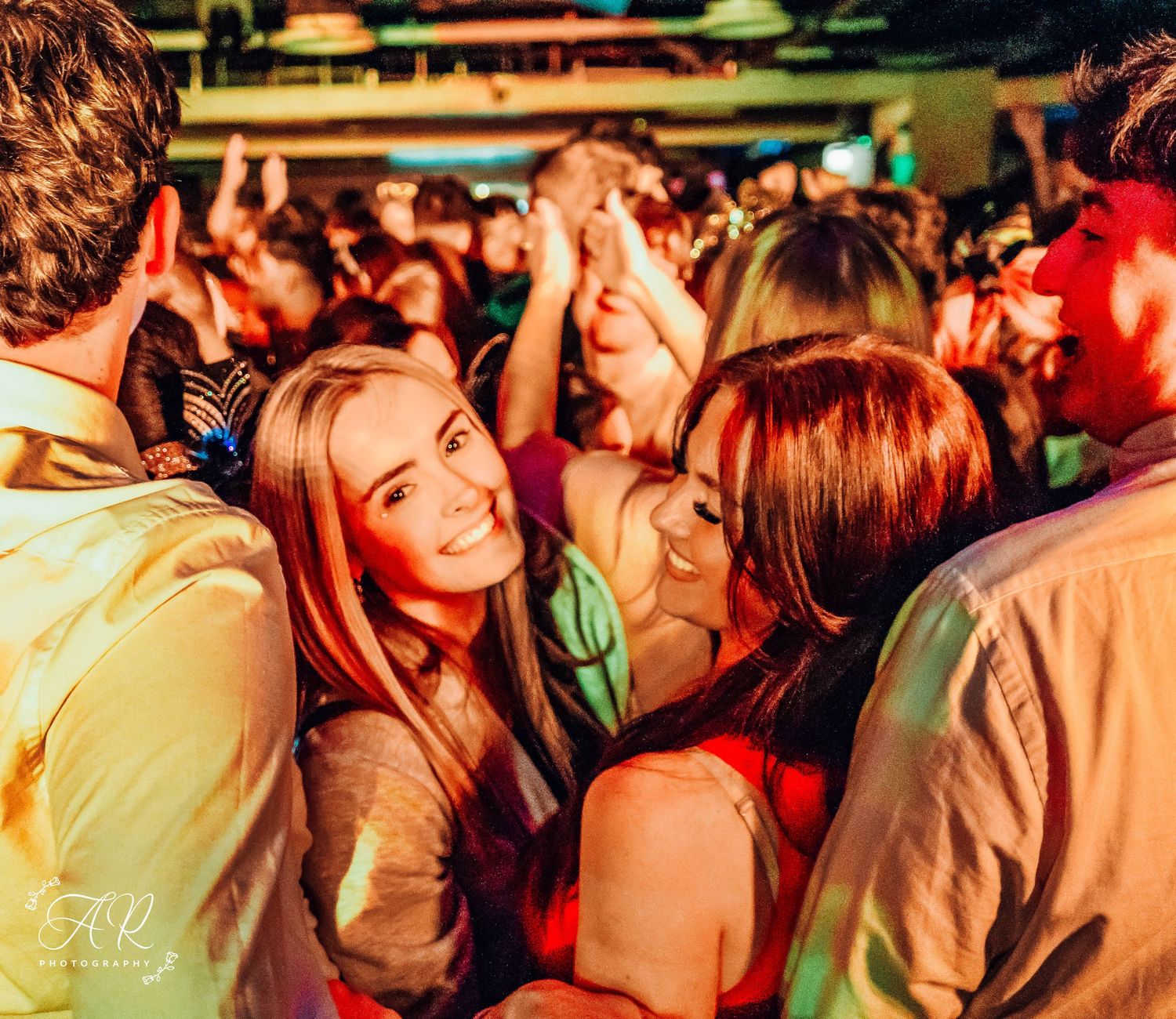 Energetic crowd enjoying themselves at a nightclub under warm ambient lighting.