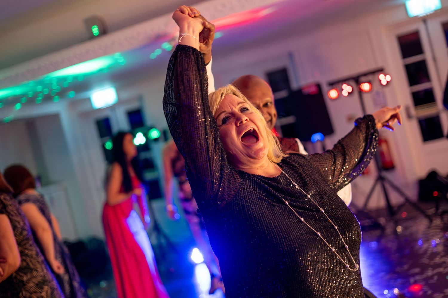 Energetic party scene with colorful lighting and people dancing in formal attire.