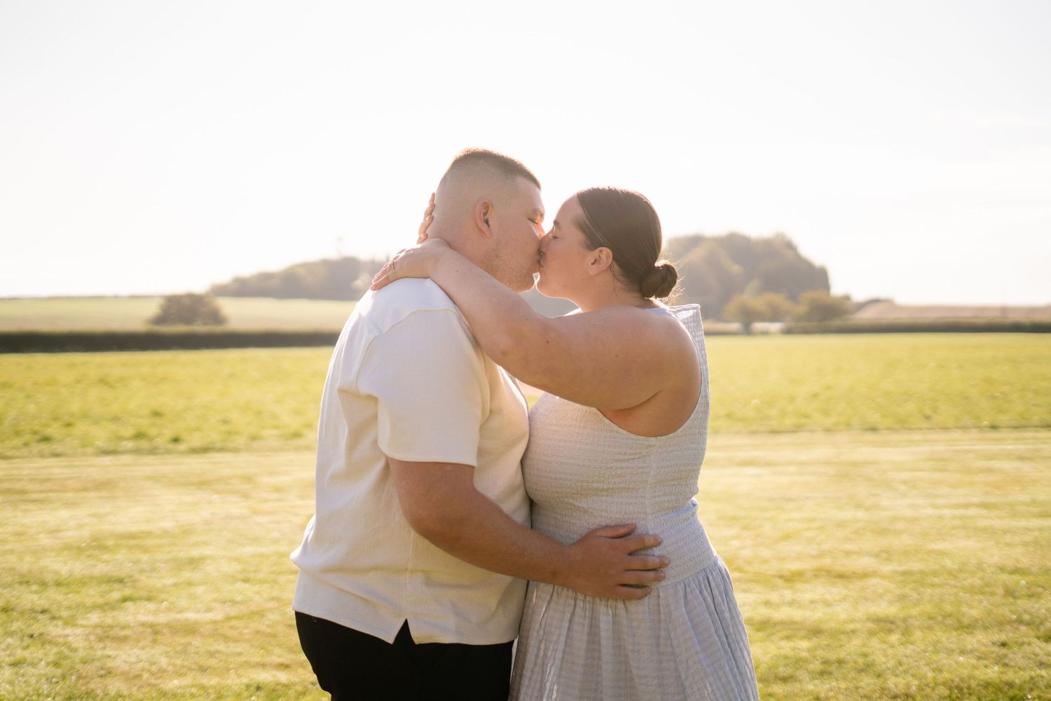 Romantic couple embraces in golden sunlight on an open field.