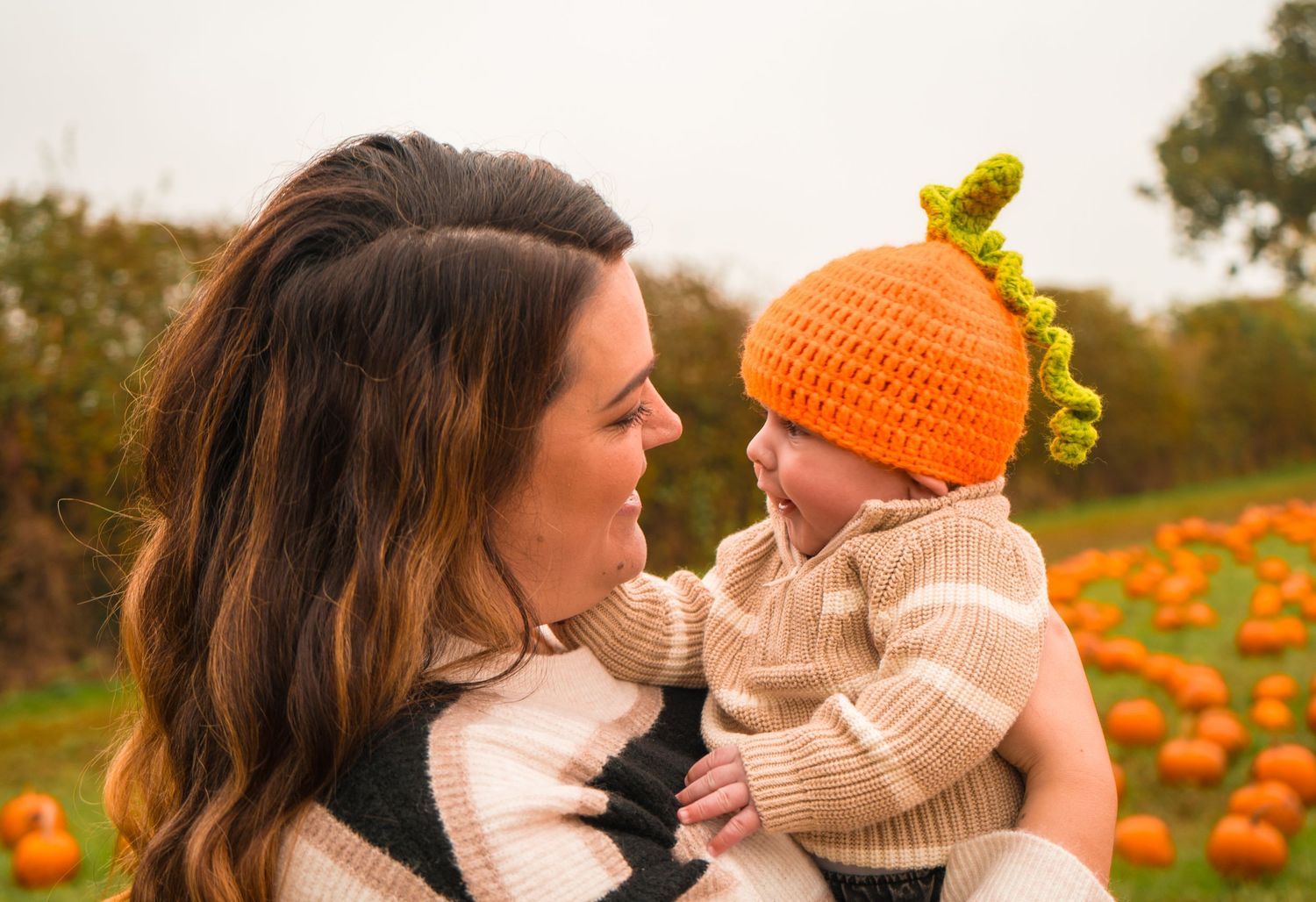 Family enjoying fall day at pumpkin patch with baby in orange knit hat.