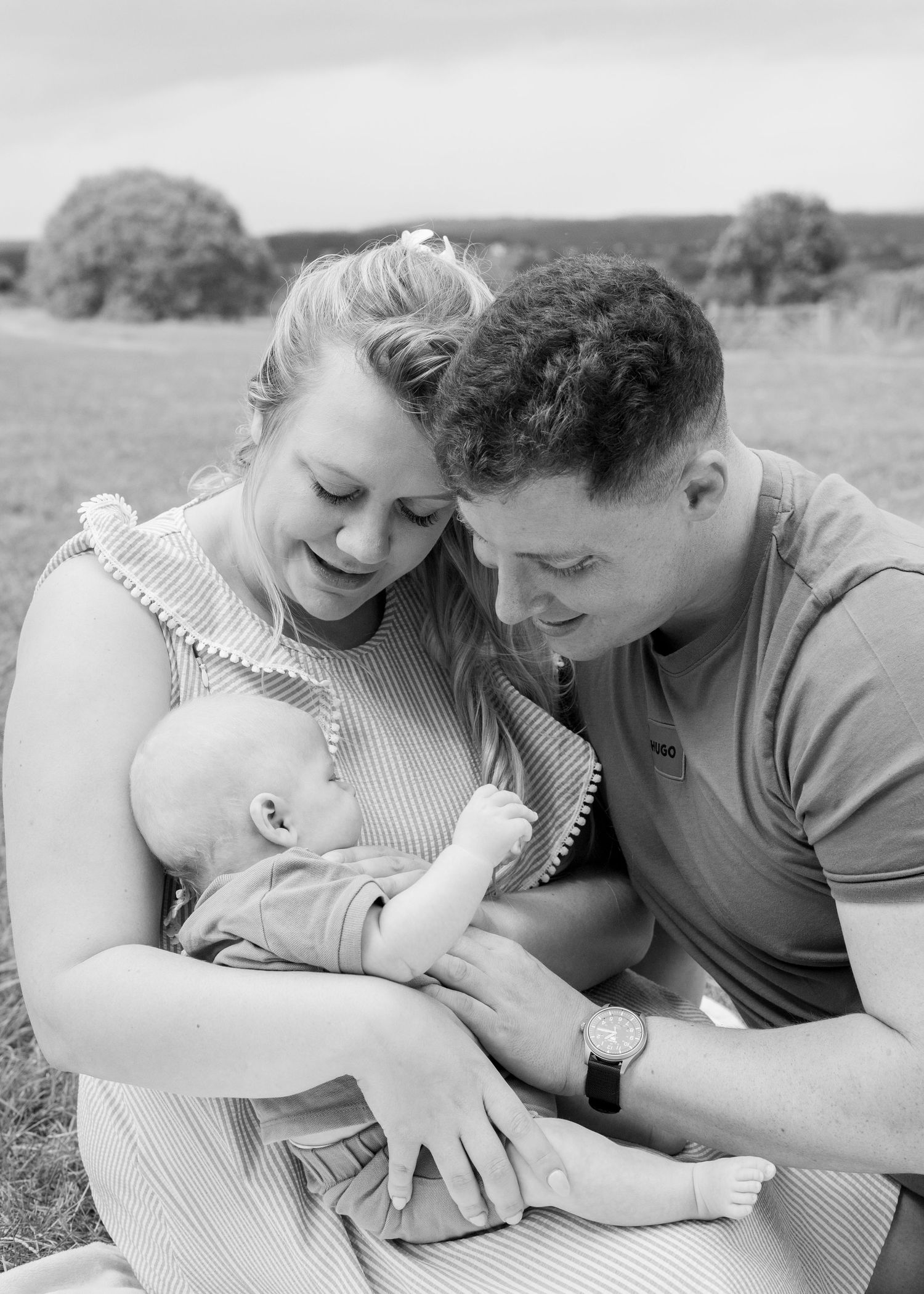 Intimate family moment captured in black and white on a sunny hillside.