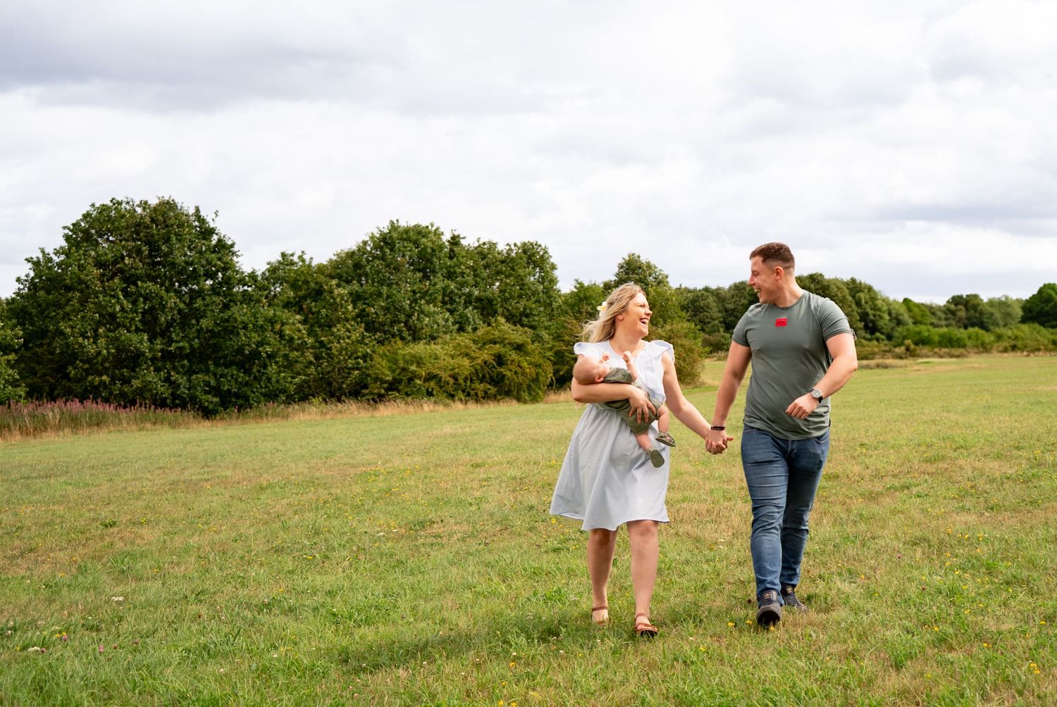 Wide landscape view of a family walking together through a green summer field.