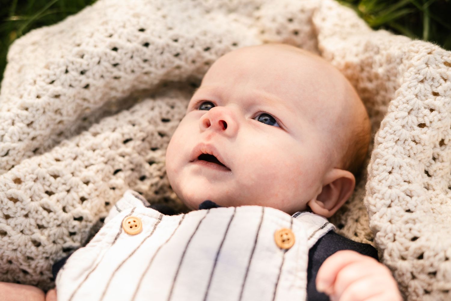 Infant lying on textured cream blanket during outdoor portrait session.