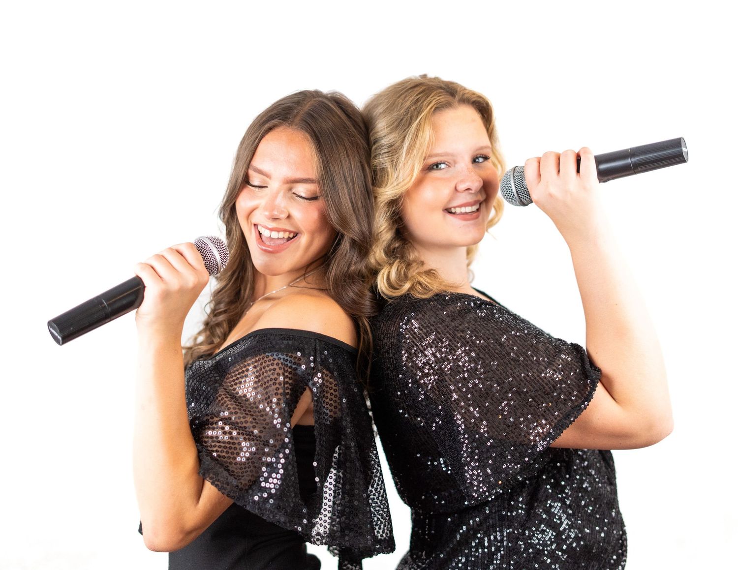 Two people in sequined black dresses posing with microphones.