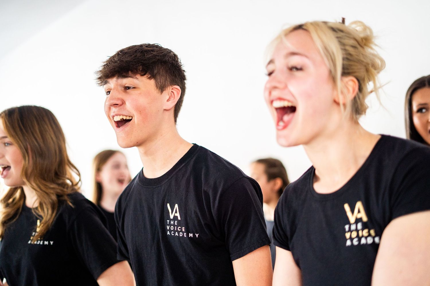 Group of dancers in black uniforms laughing and practicing together in a bright studio space.