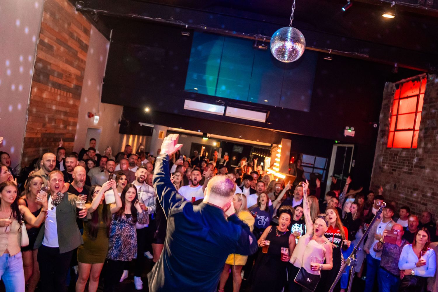 Crowded music venue with disco ball and colored lighting during live performance.