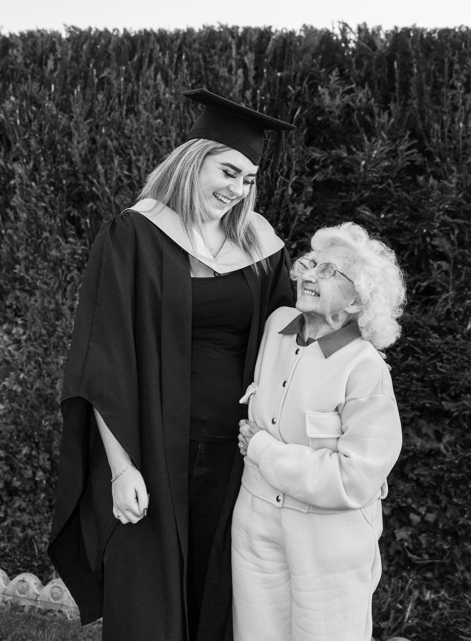 Graduate in academic regalia sharing a moment with an elderly person outdoors.