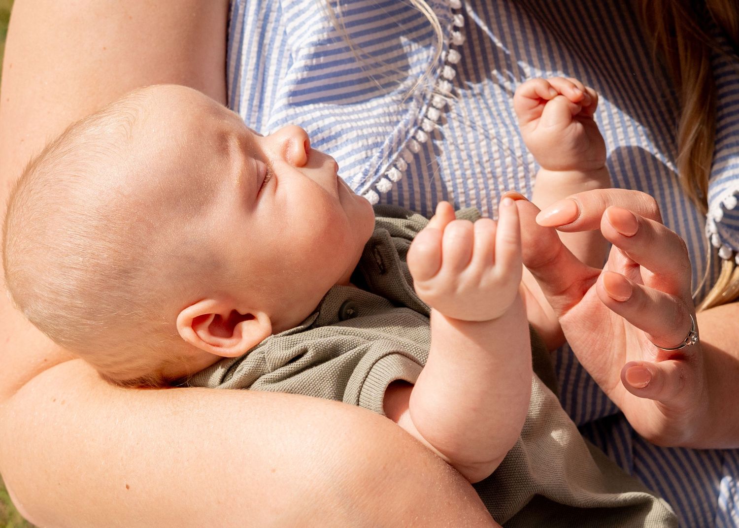 Baby lying on back reaching up with tiny hands in sunlit moment.