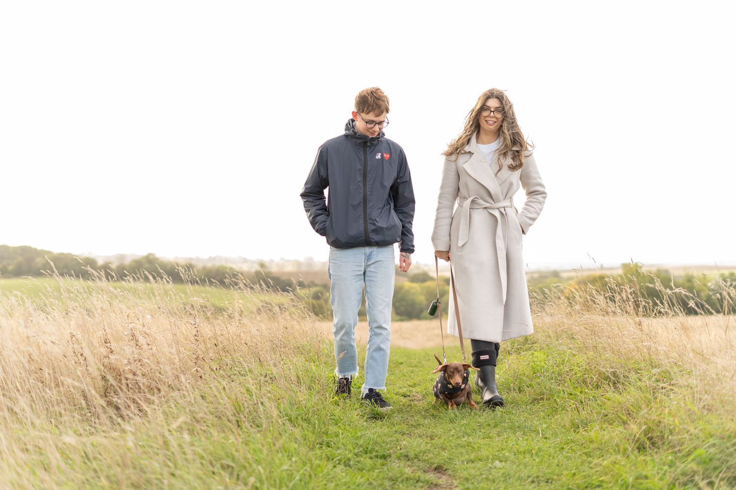 Couple walking with their dachshund puppy through a golden autumn field.