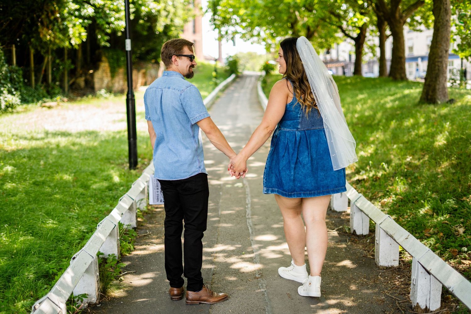 A couple walking together on a tree-lined path on a sunny day.