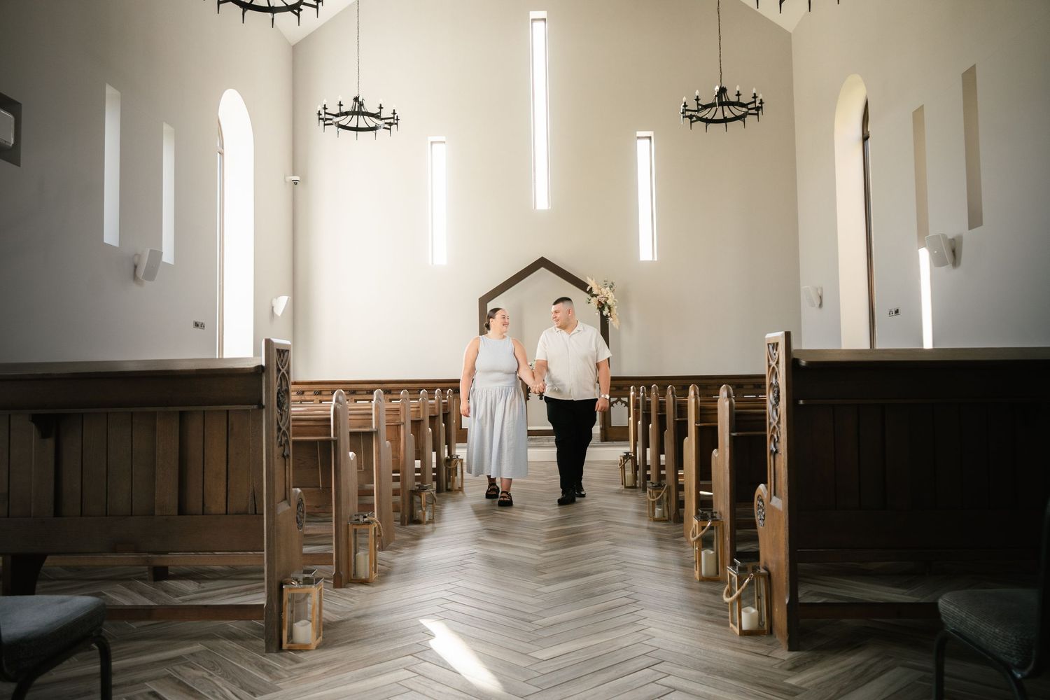 Bright white church sanctuary with wooden pews and contemporary chandeliers hanging from vaulted ceiling.