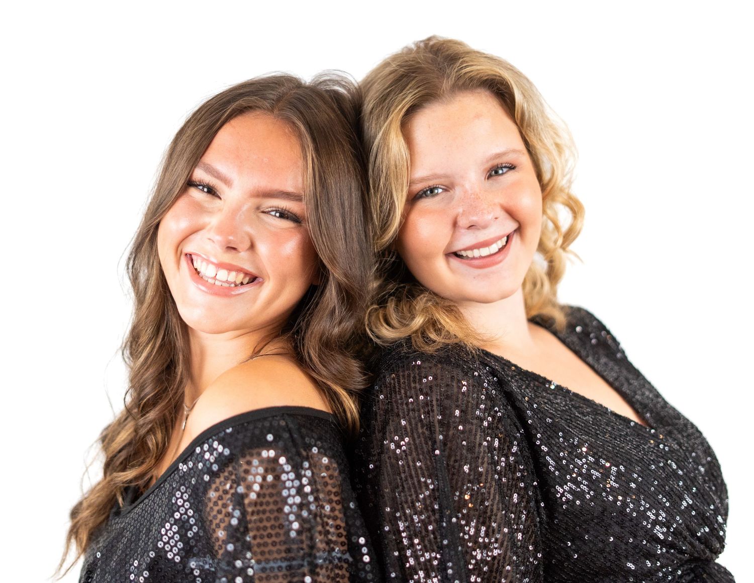 Two performers in black sequined tops share a joyful moment during a photoshoot.