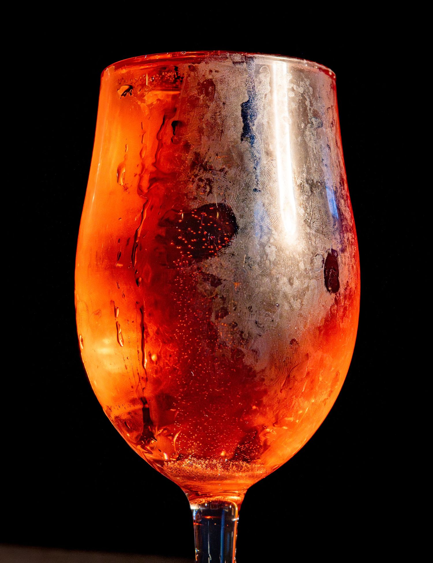 A wine glass filled with a reddish-orange beverage showing condensation on the glass surface.