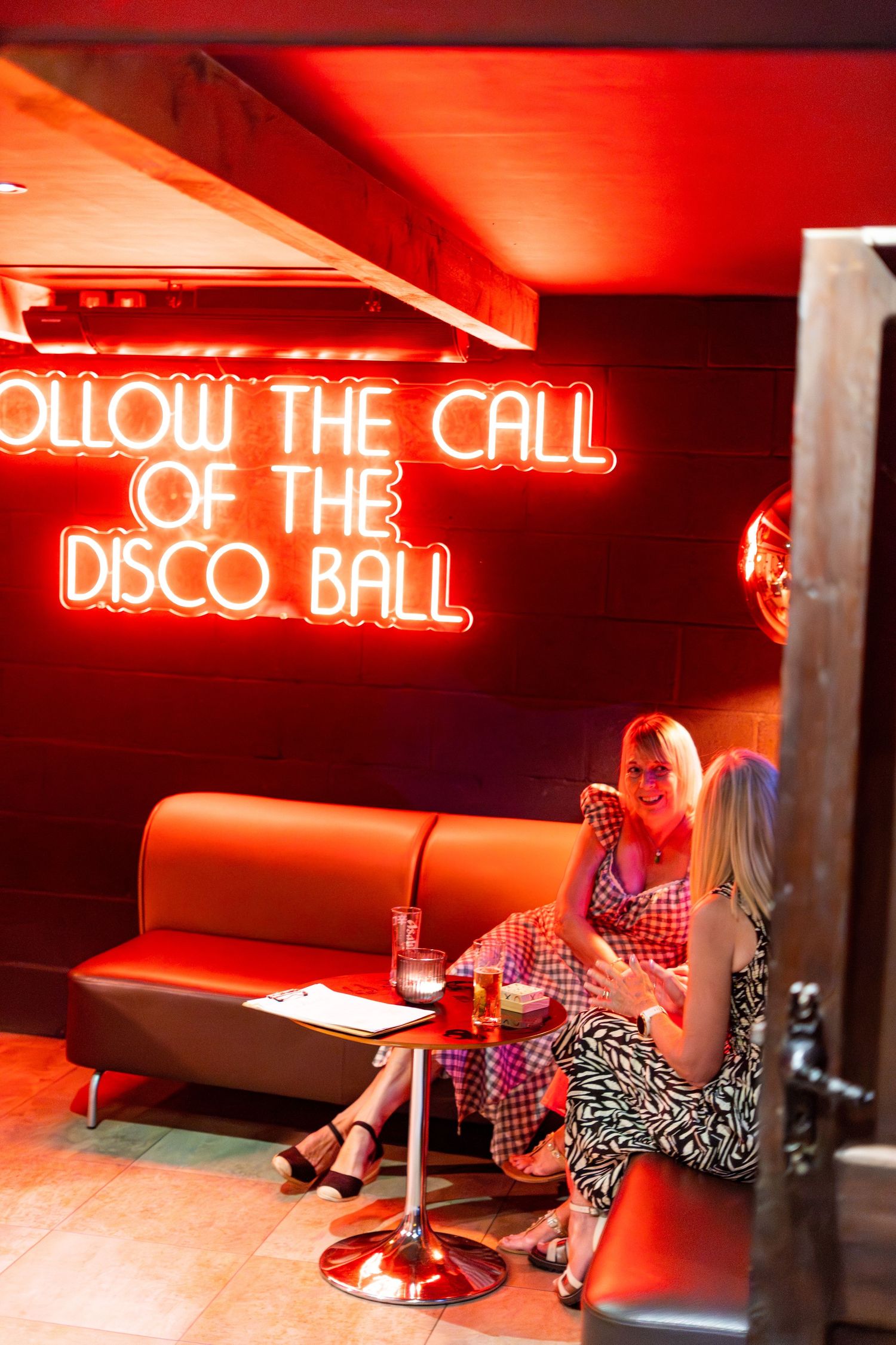 Red neon signage illuminates a lounge area with booth seating.