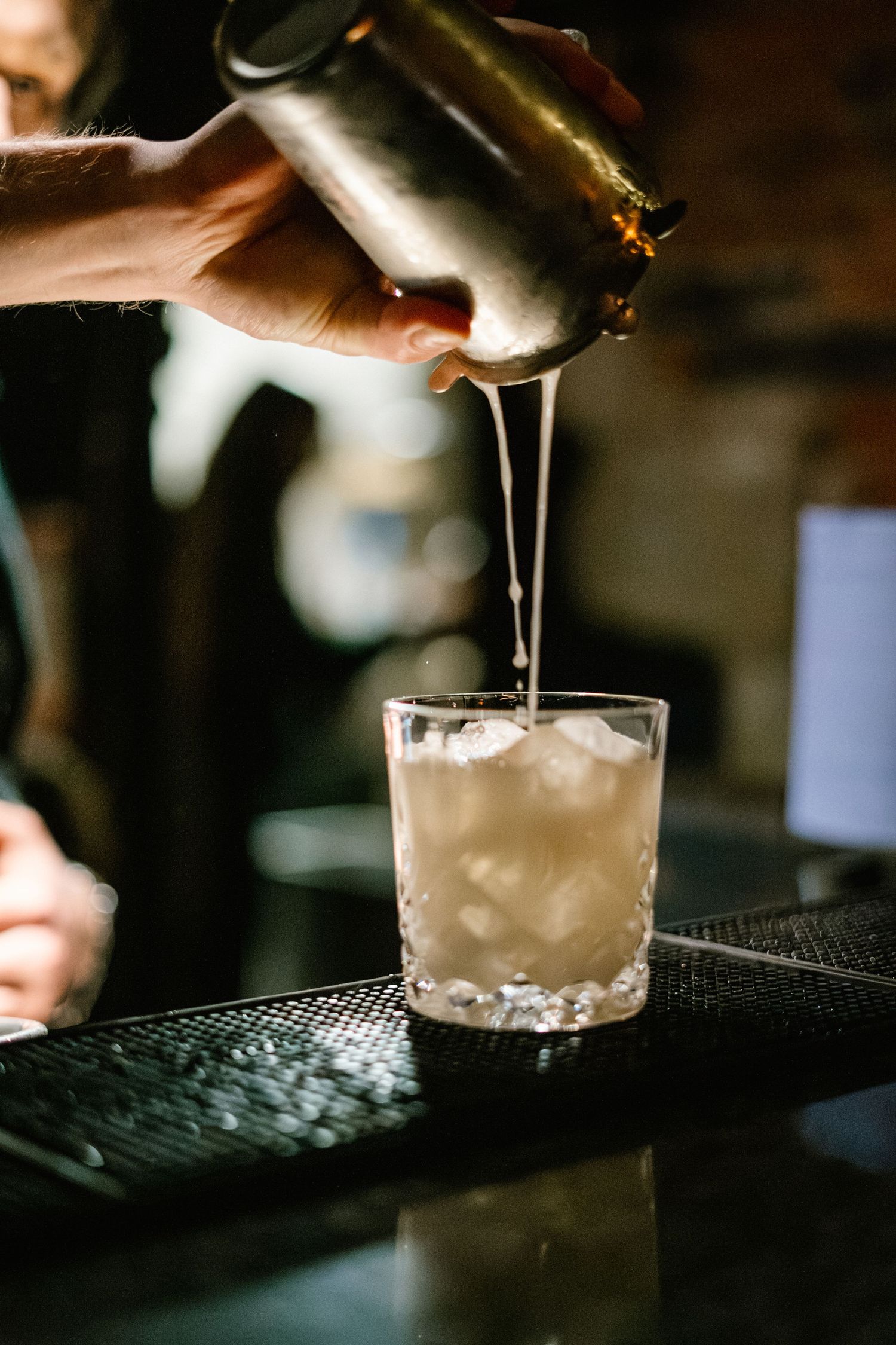 Pouring a creamy white cocktail from a shaker into a rocks glass.