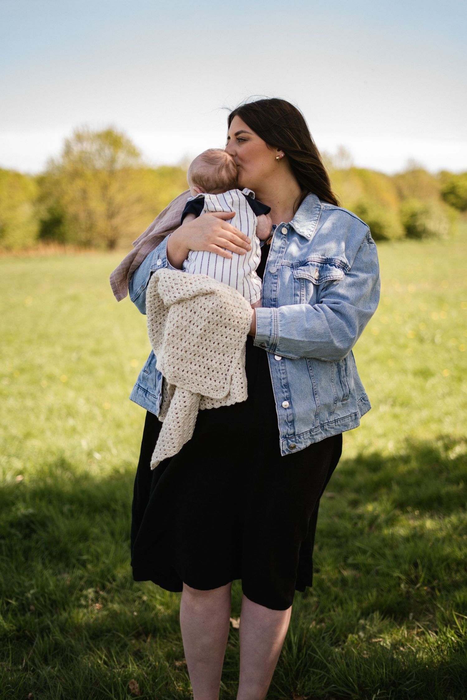 Multiple shots of someone in denim jacket holding a blanket-wrapped baby in a field.