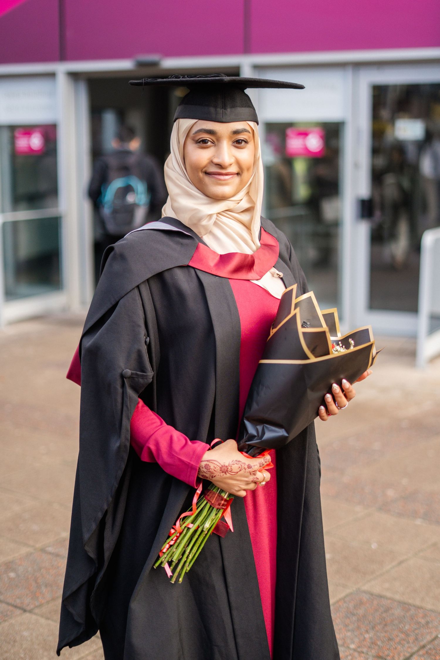 Graduate in traditional academic dress holds diploma and flowers during celebration.