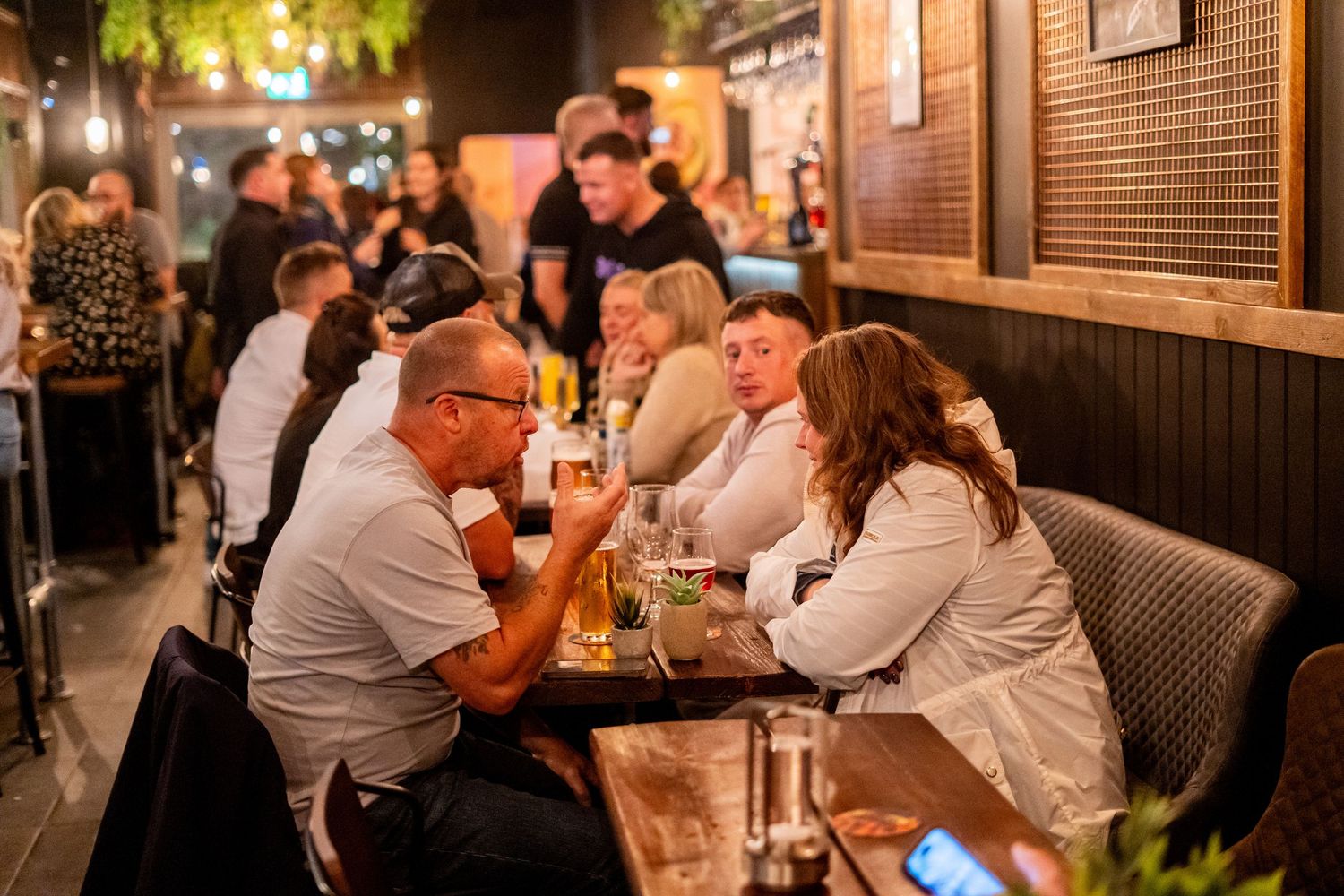 Restaurant patrons enjoying conversation and drinks at tables in dimly lit dining area.