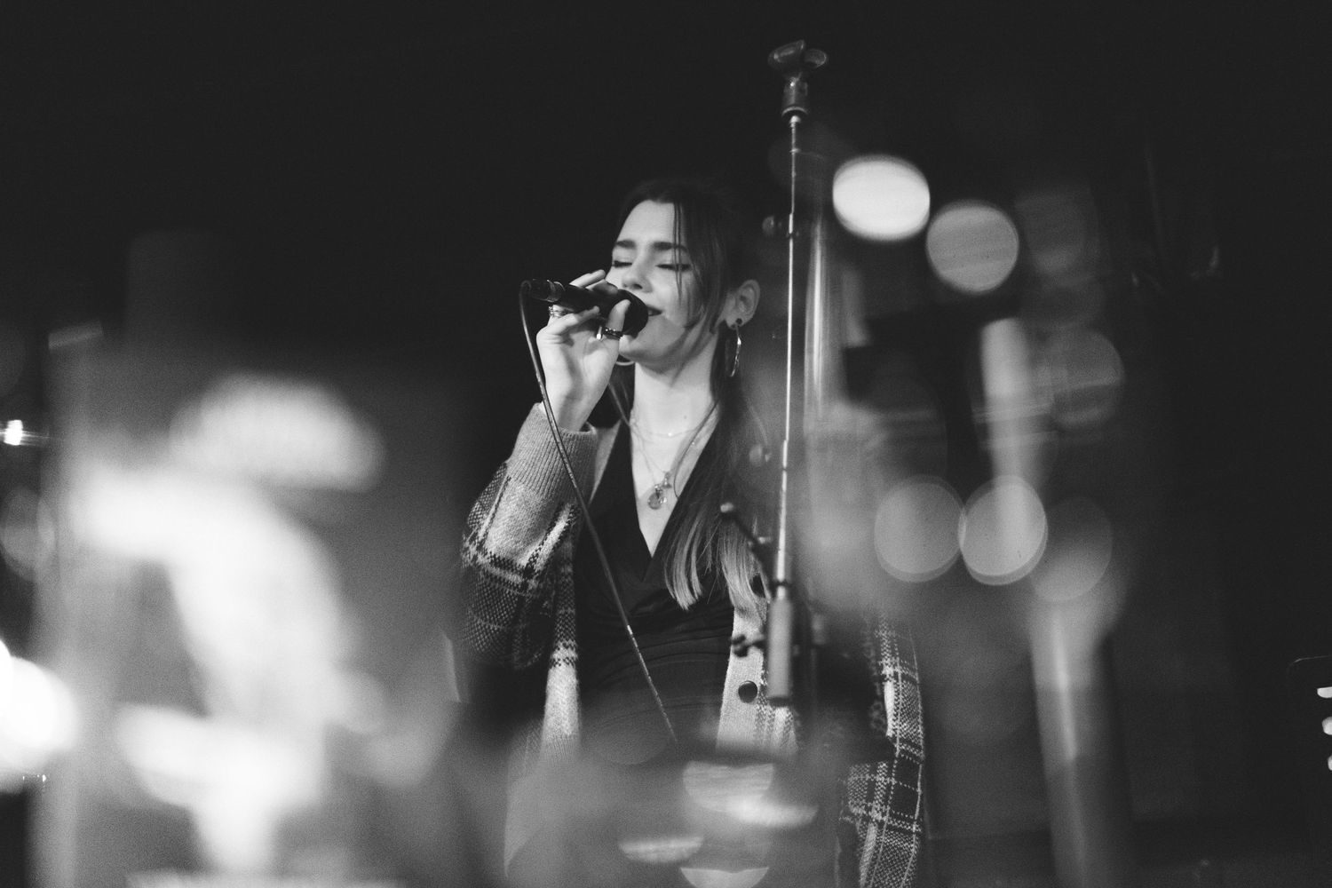A black and white concert photo showing a performer at a microphone with blurred lights.