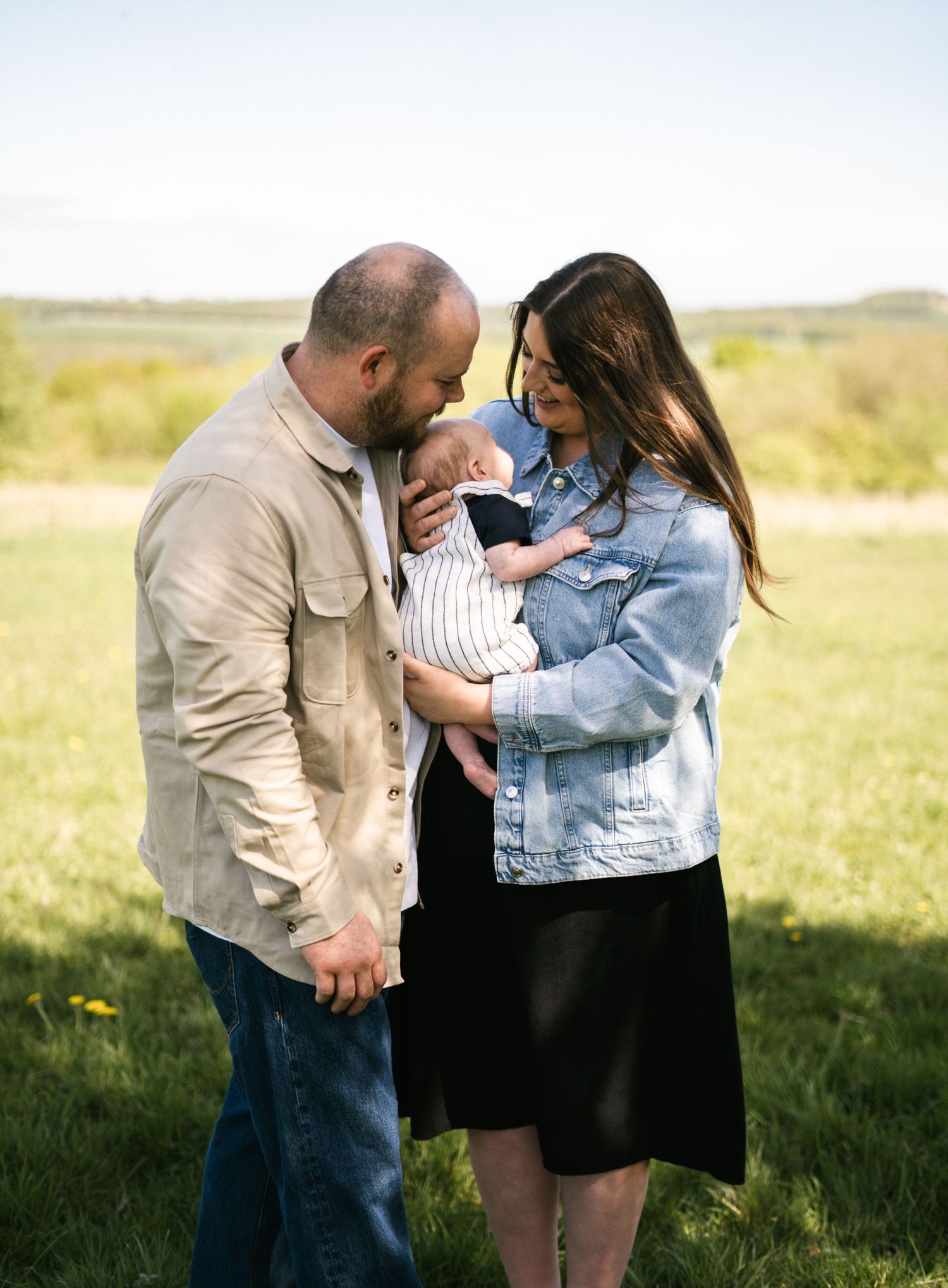 Family of three sharing an intimate moment together in a sunny meadow.