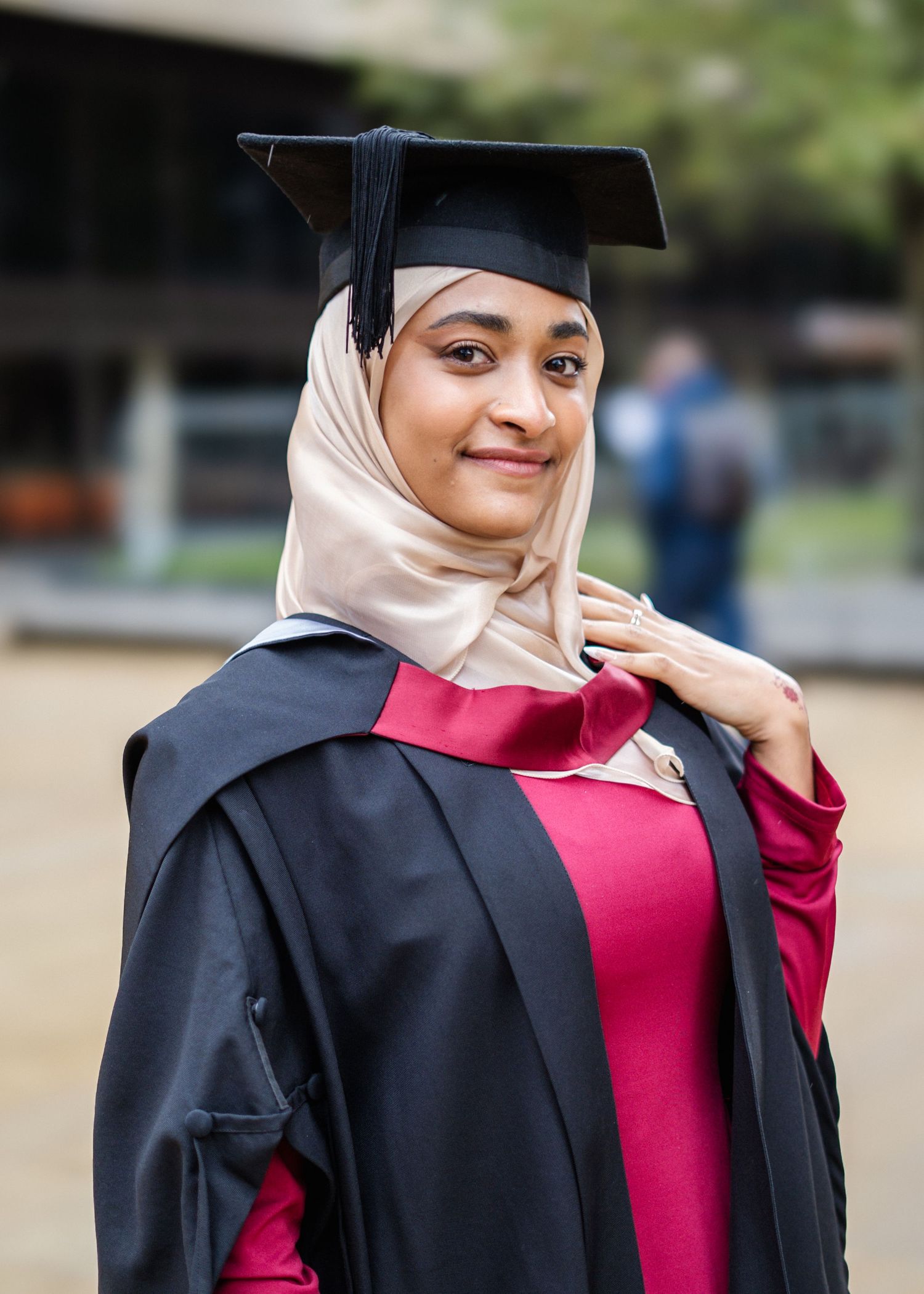 Graduate in black academic regalia and red dress poses with graduation cap.