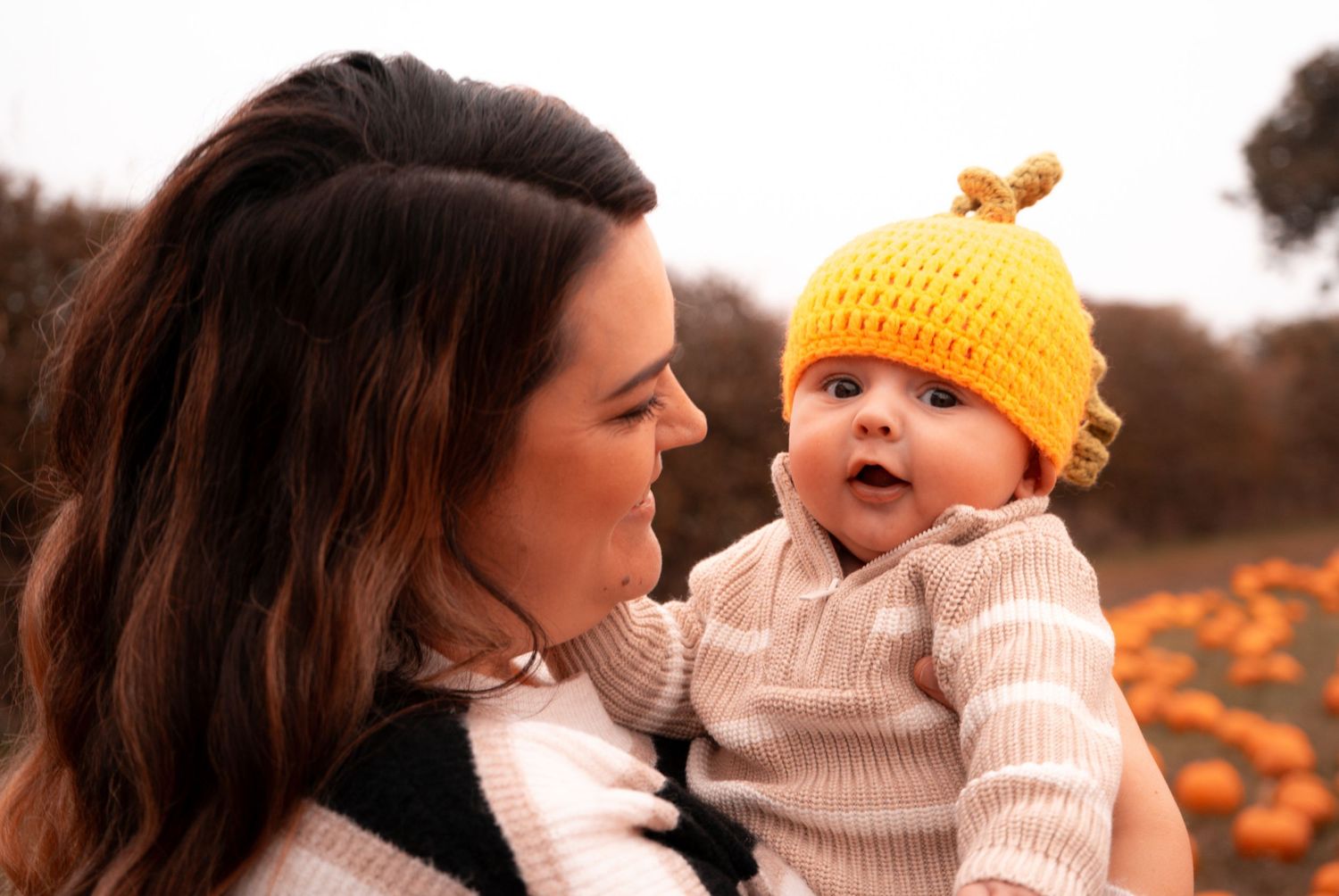 Parent and baby in matching autumn outfits share joyful moment at pumpkin patch.