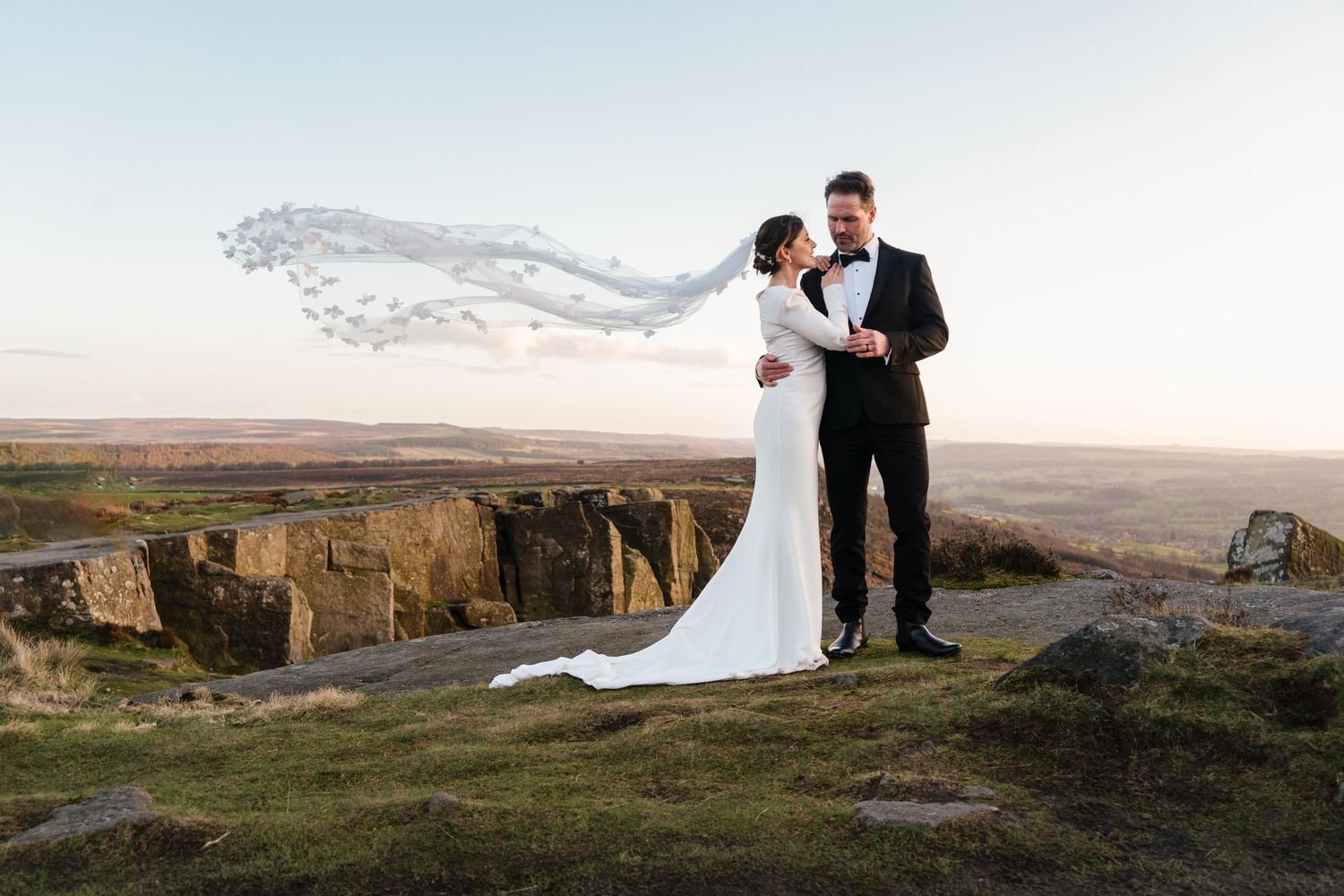 Couple shares an intimate moment against a dramatic cliffside landscape at sunset.